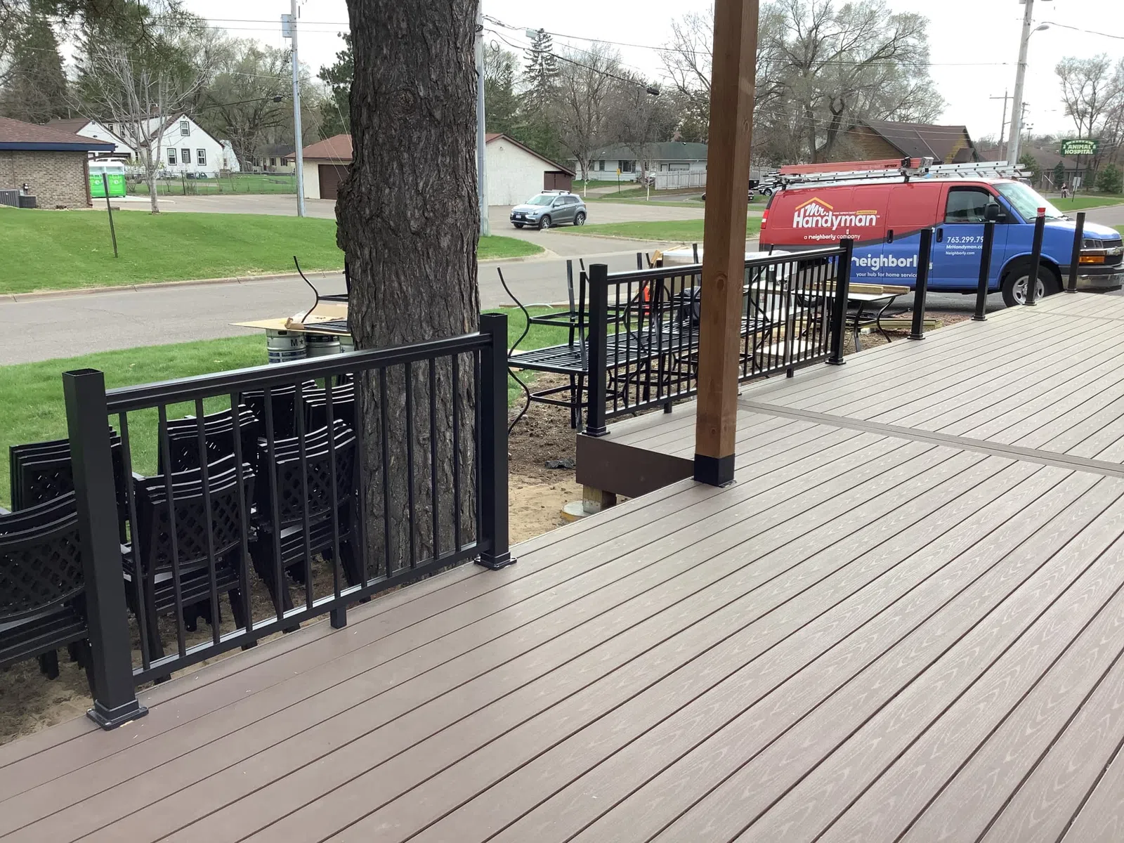 Spacious wooden deck with black metal railing, tree, and a red Mr. Handyman van parked on the street nearby.