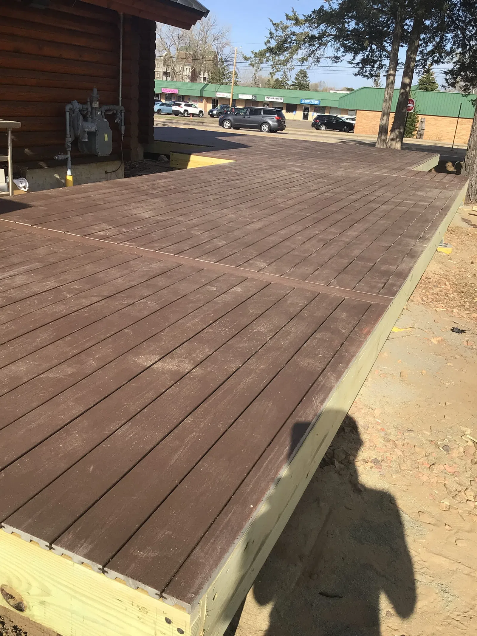 Newly constructed elevated wooden deck attached to a log cabin with nearby parking and trees.