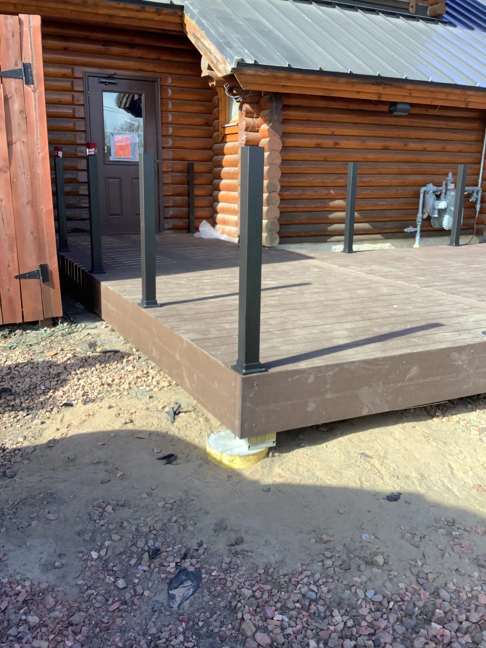 Newly constructed brown wooden deck with black metal posts attached to a log cabin exterior door.