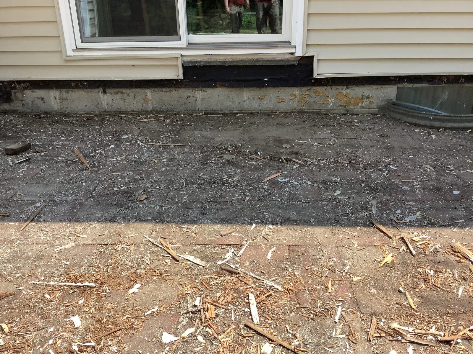 Cleared backyard ground with dirt and wood debris outside a house with beige siding and sliding glass door.