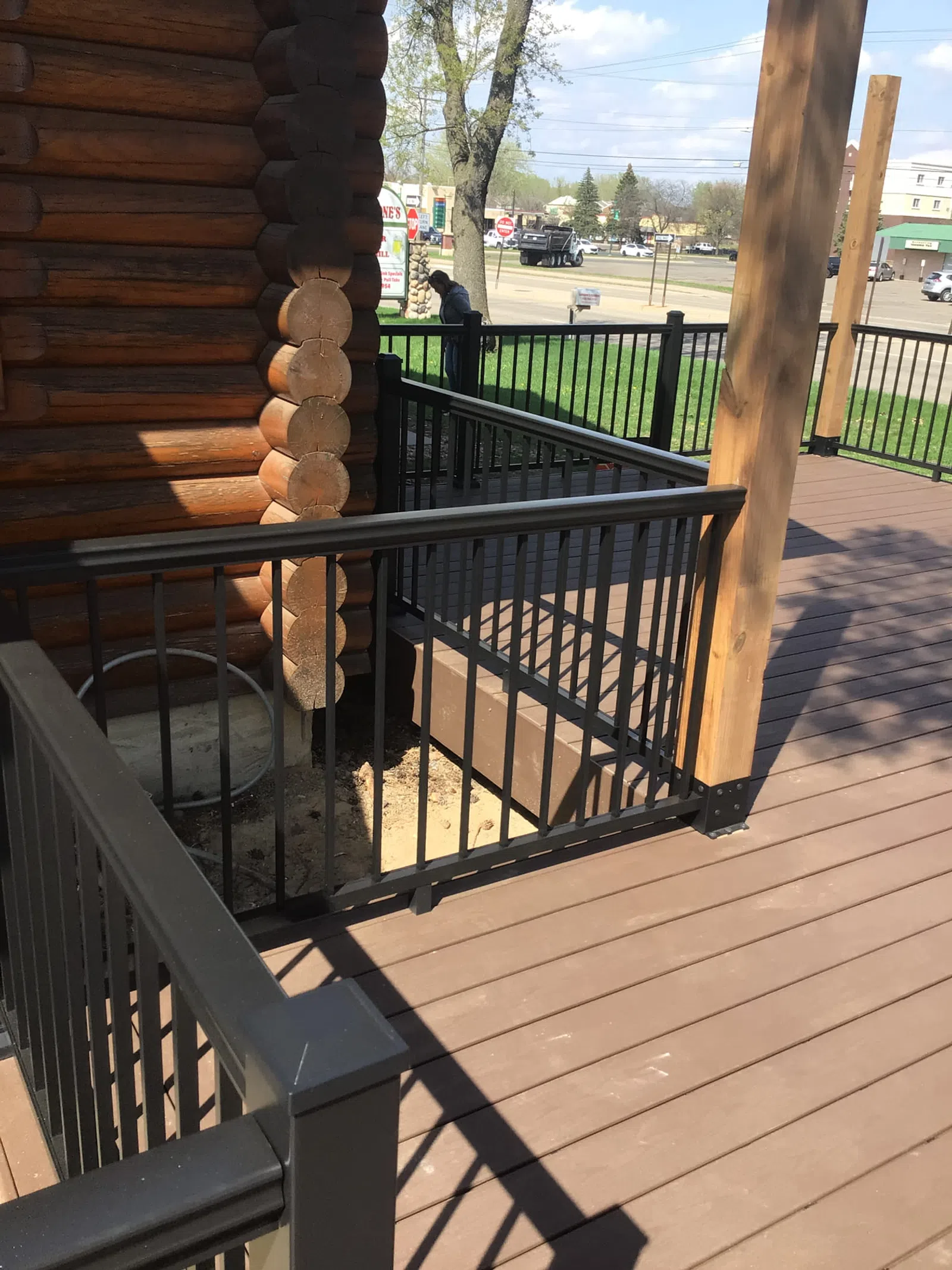 Brown wooden deck with black metal railing and part of a log cabin under clear daylight.