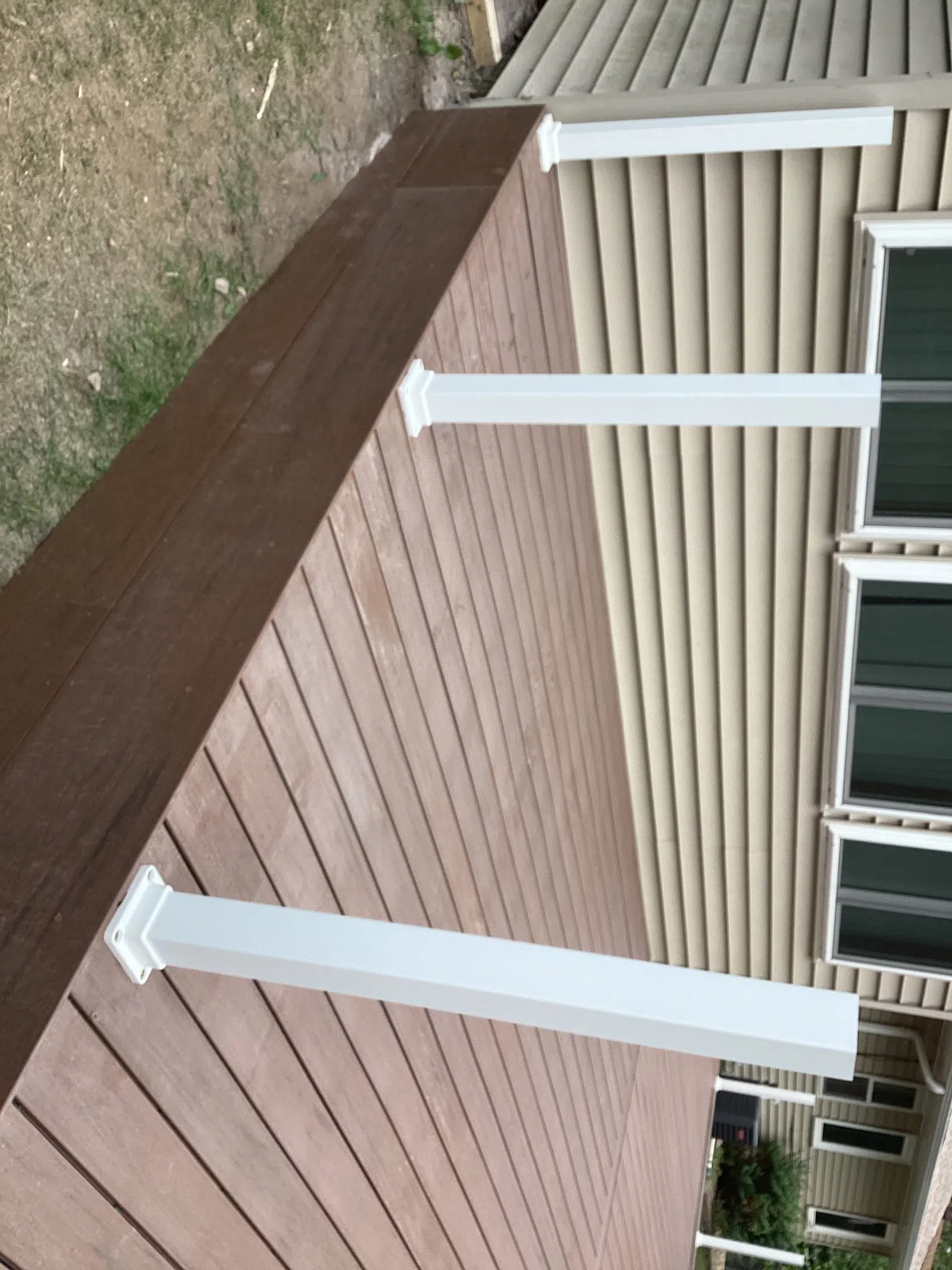 Newly built brown wooden deck attached to beige house with white support posts and large windows.