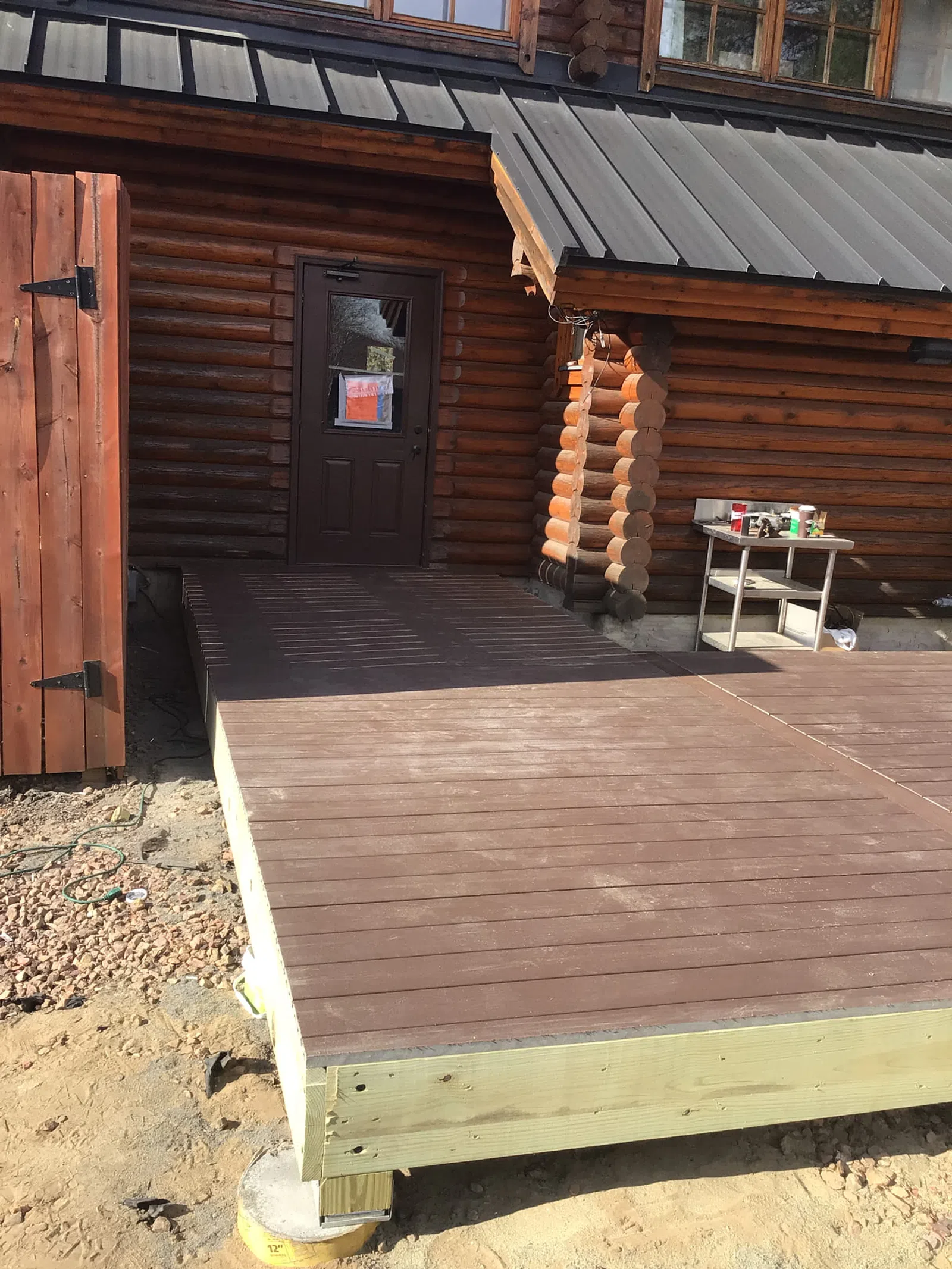 Newly built raised wooden deck attached to a rustic log cabin with a metal roof and a dark door.