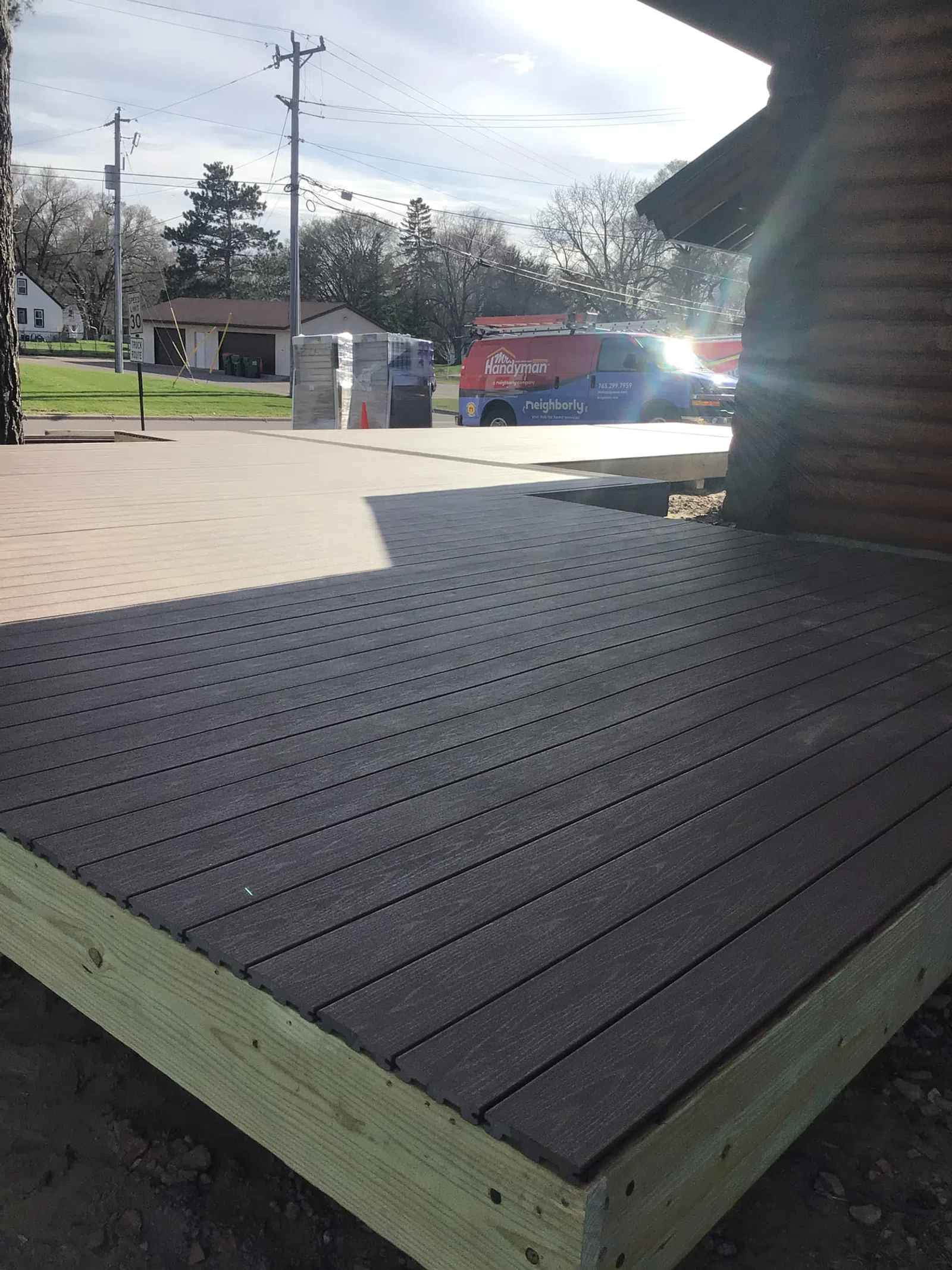 Newly constructed two-tone wood deck outside a log cabin with a handyman service van in the background.