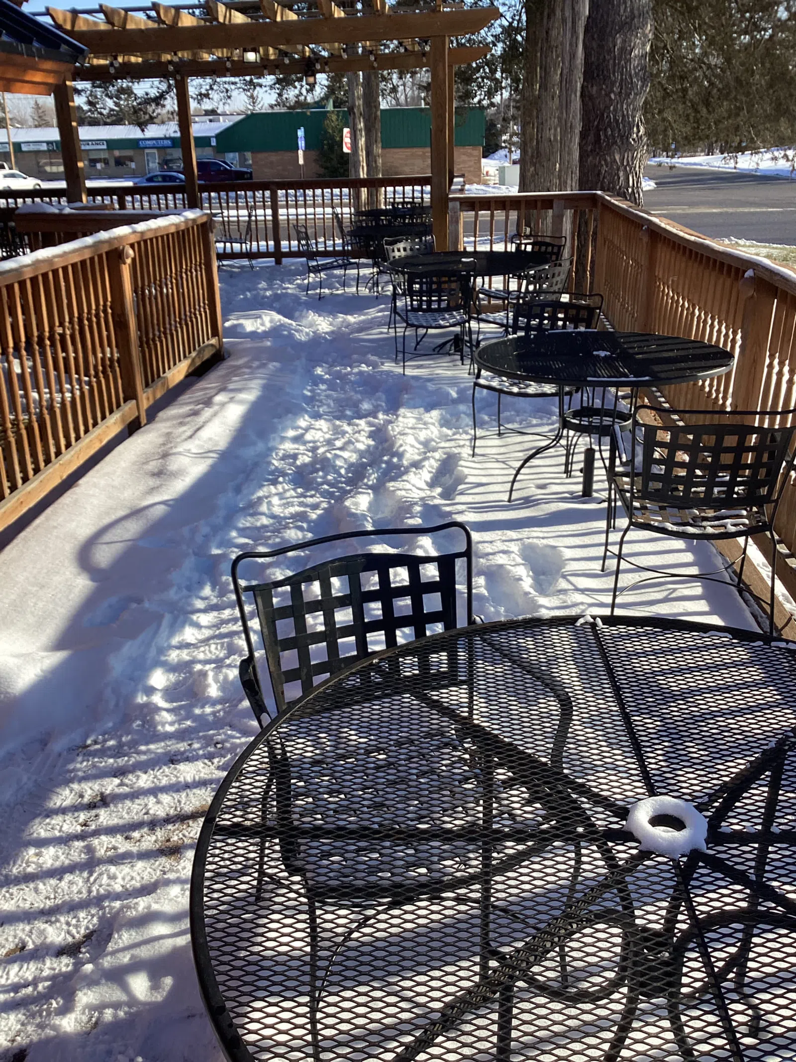 Outdoor patio with black metal tables and chairs covered in snow on a sunny winter day.