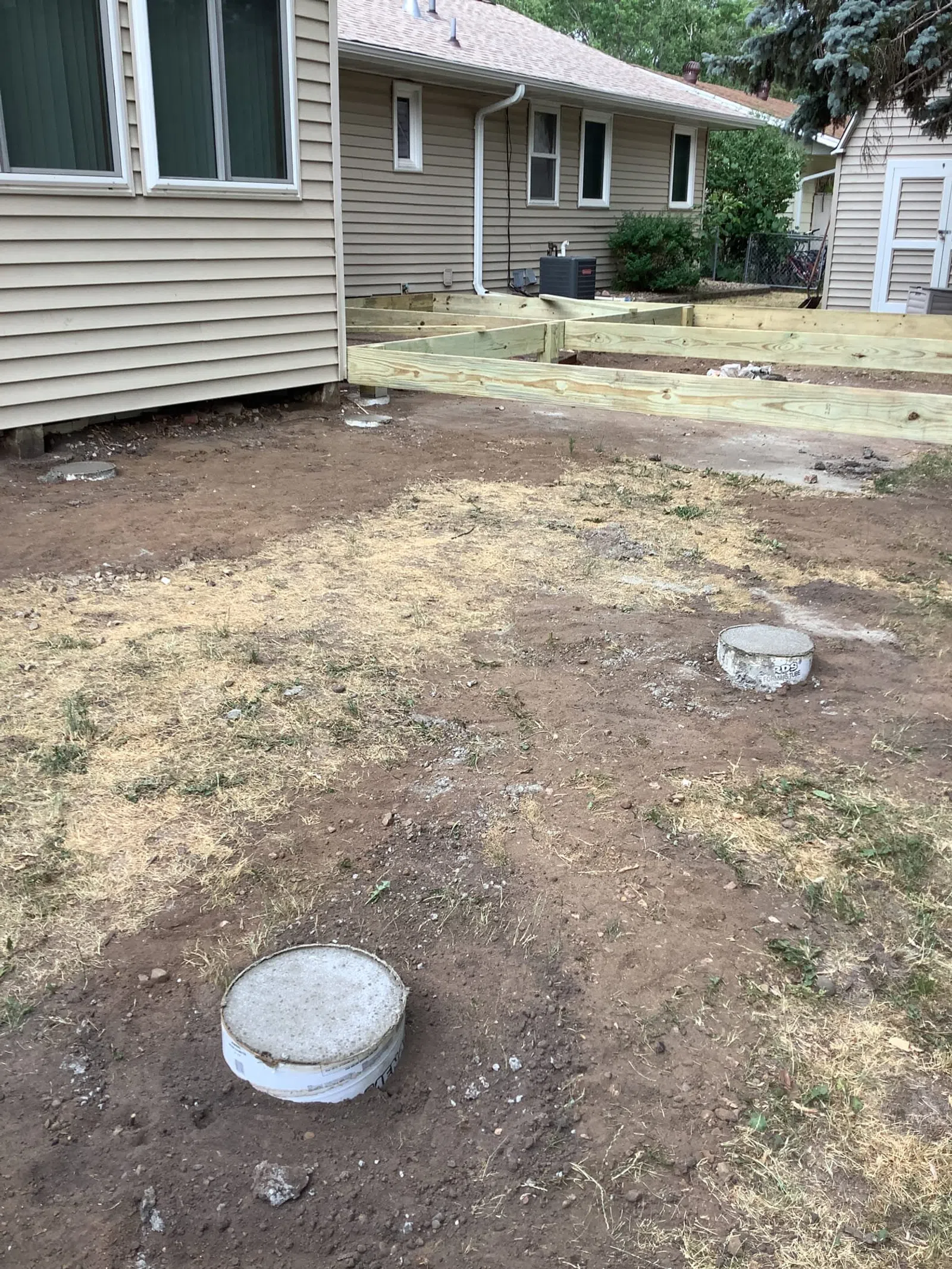 New wooden deck frame constructed beside house with concrete piers in grassy backyard under construction.