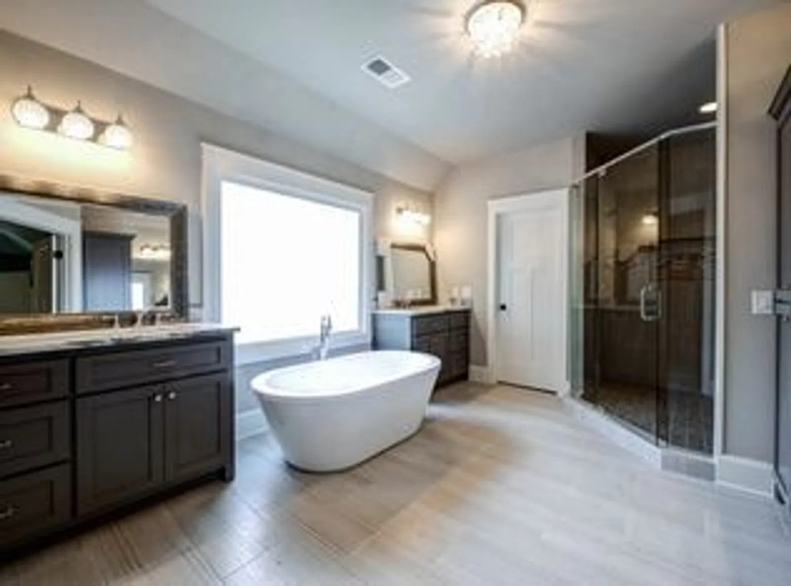 Modern bathroom with freestanding tub, dual vanities, large window, and glass-enclosed shower with tiled floor.
