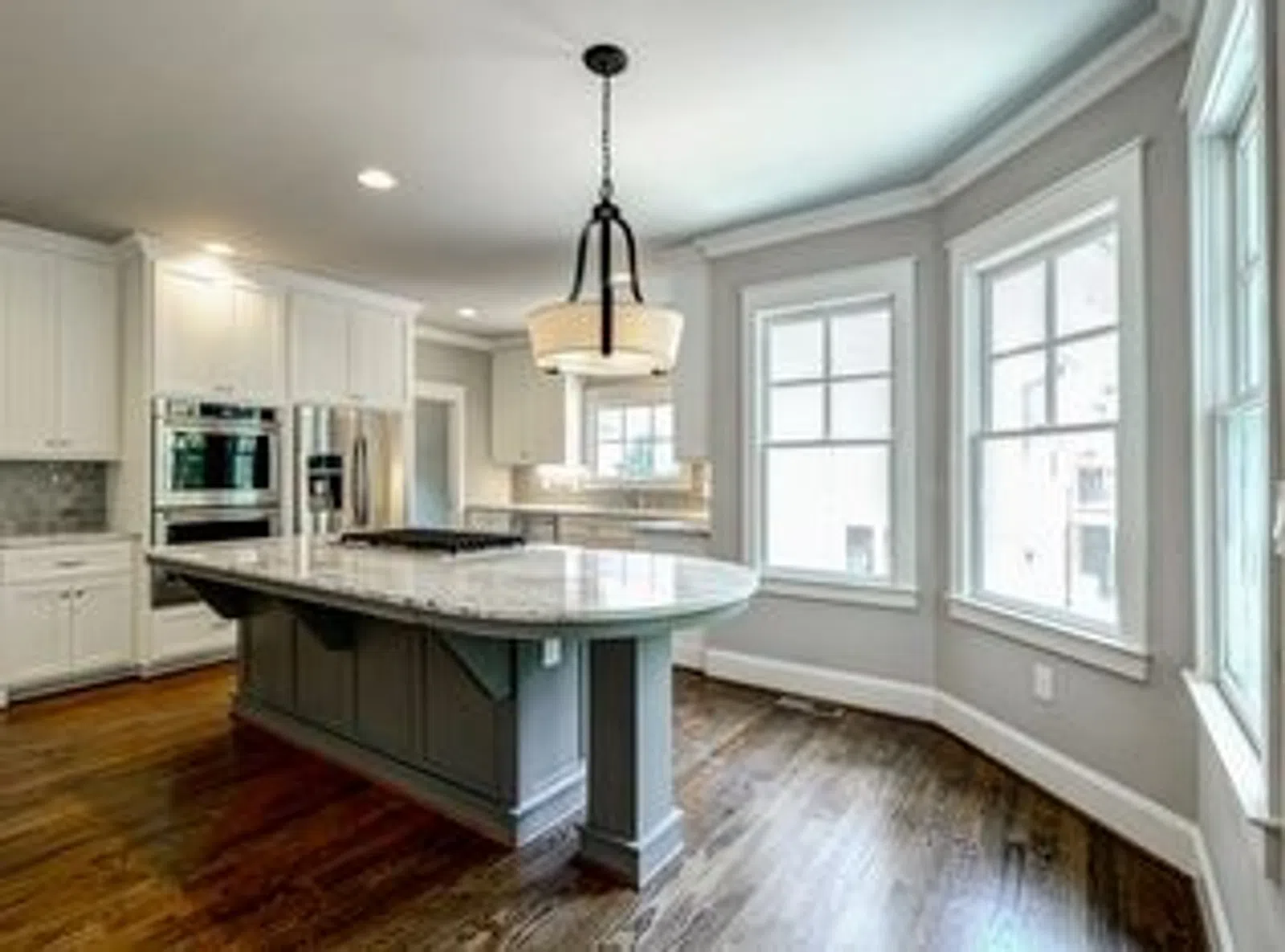 Bright modern kitchen with large marble island, white cabinets, stainless steel appliances, hardwood floors, and large windows