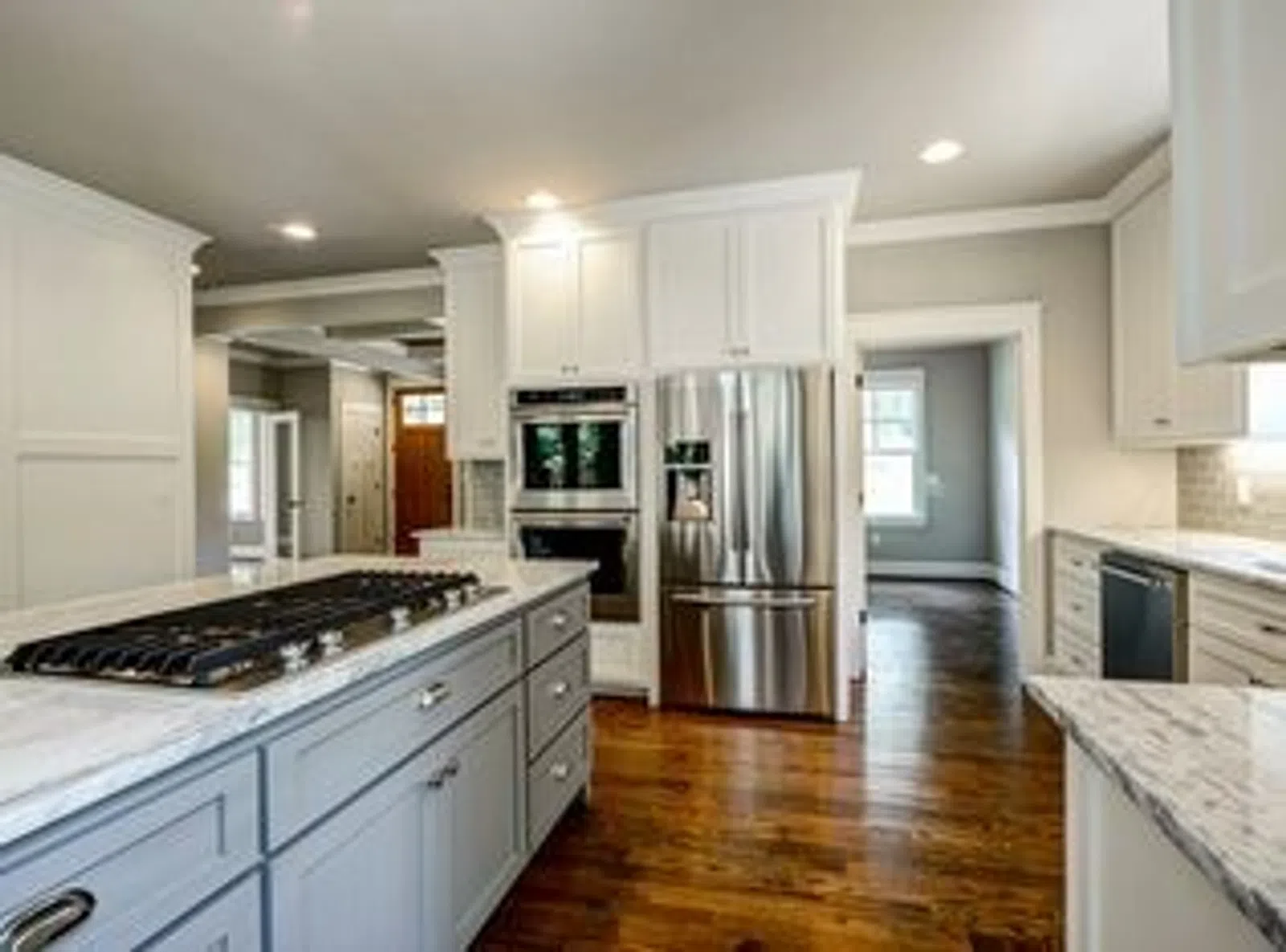 Modern kitchen with gray island, white cabinets, stainless steel appliances, and hardwood flooring in open layout