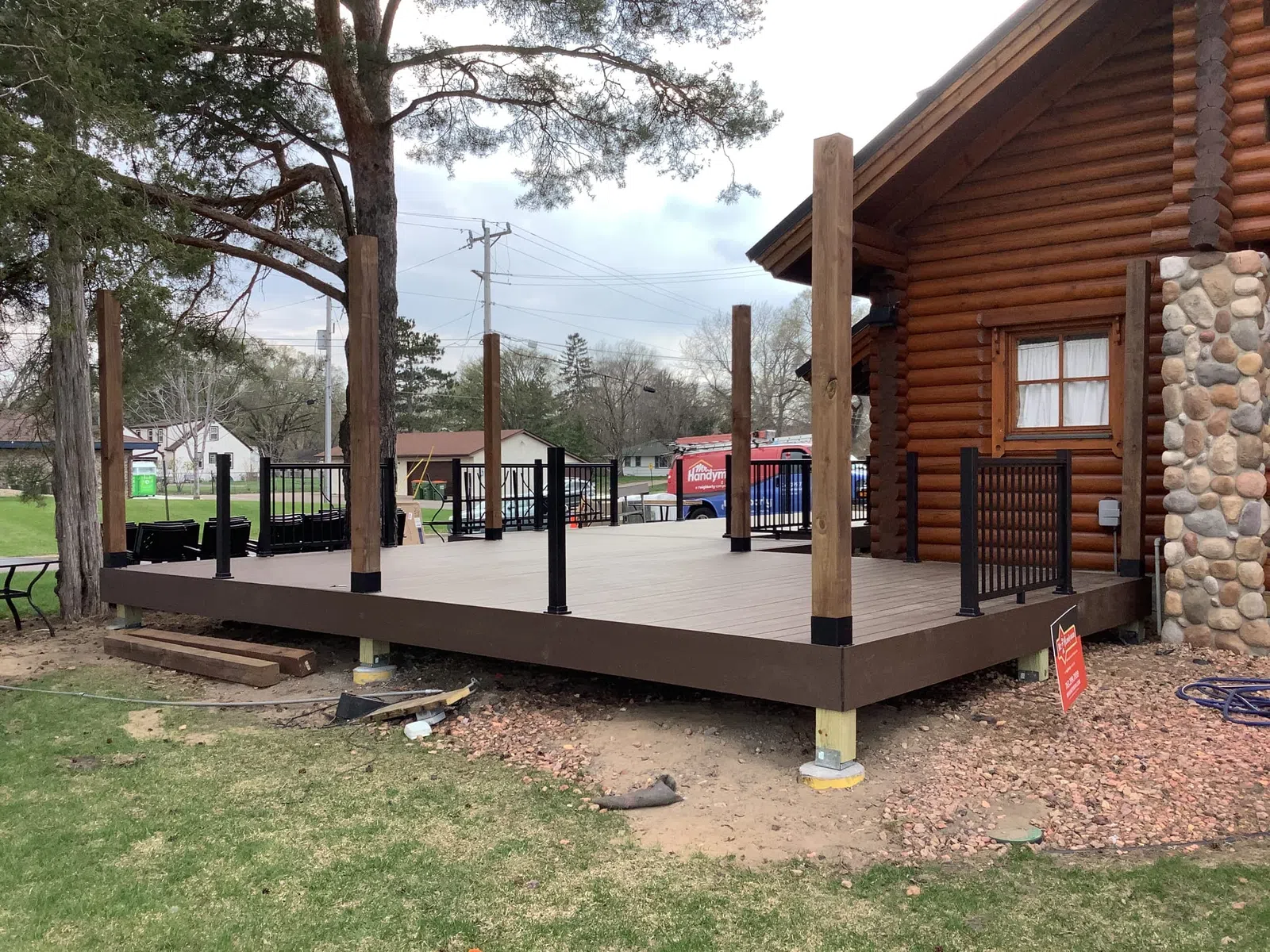 Partially constructed wooden deck attached to a log cabin with black railings and vertical posts on a cloudy day.
