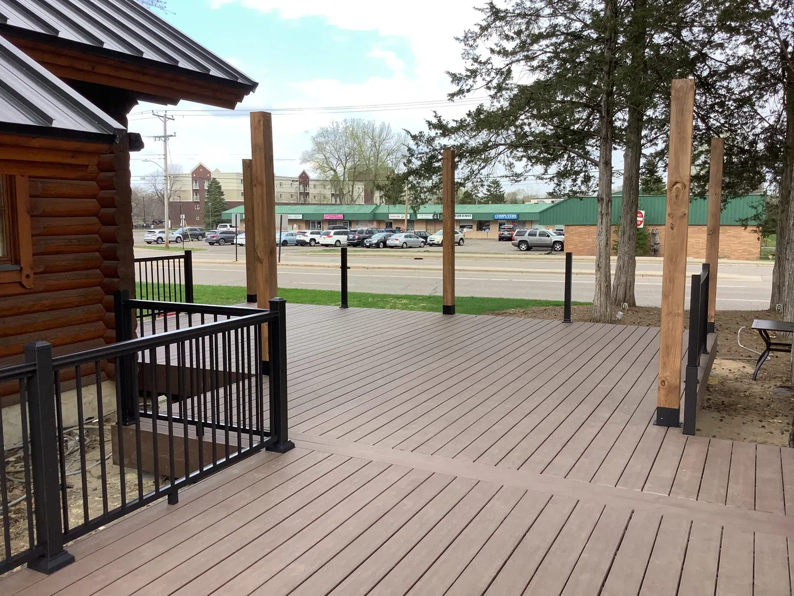 Spacious wooden deck with black metal railings and vertical posts next to a log cabin under a blue sky.