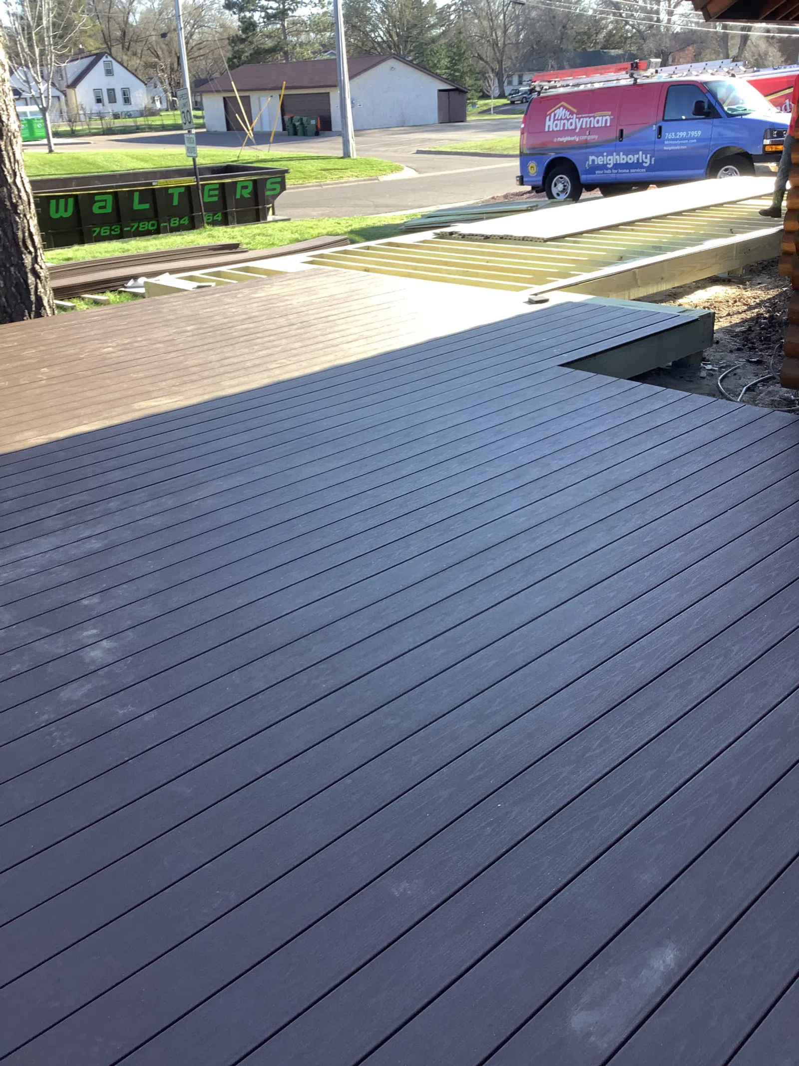 View of a newly constructed dark wood deck and an unfinished section under construction with a handyman service van nearby.