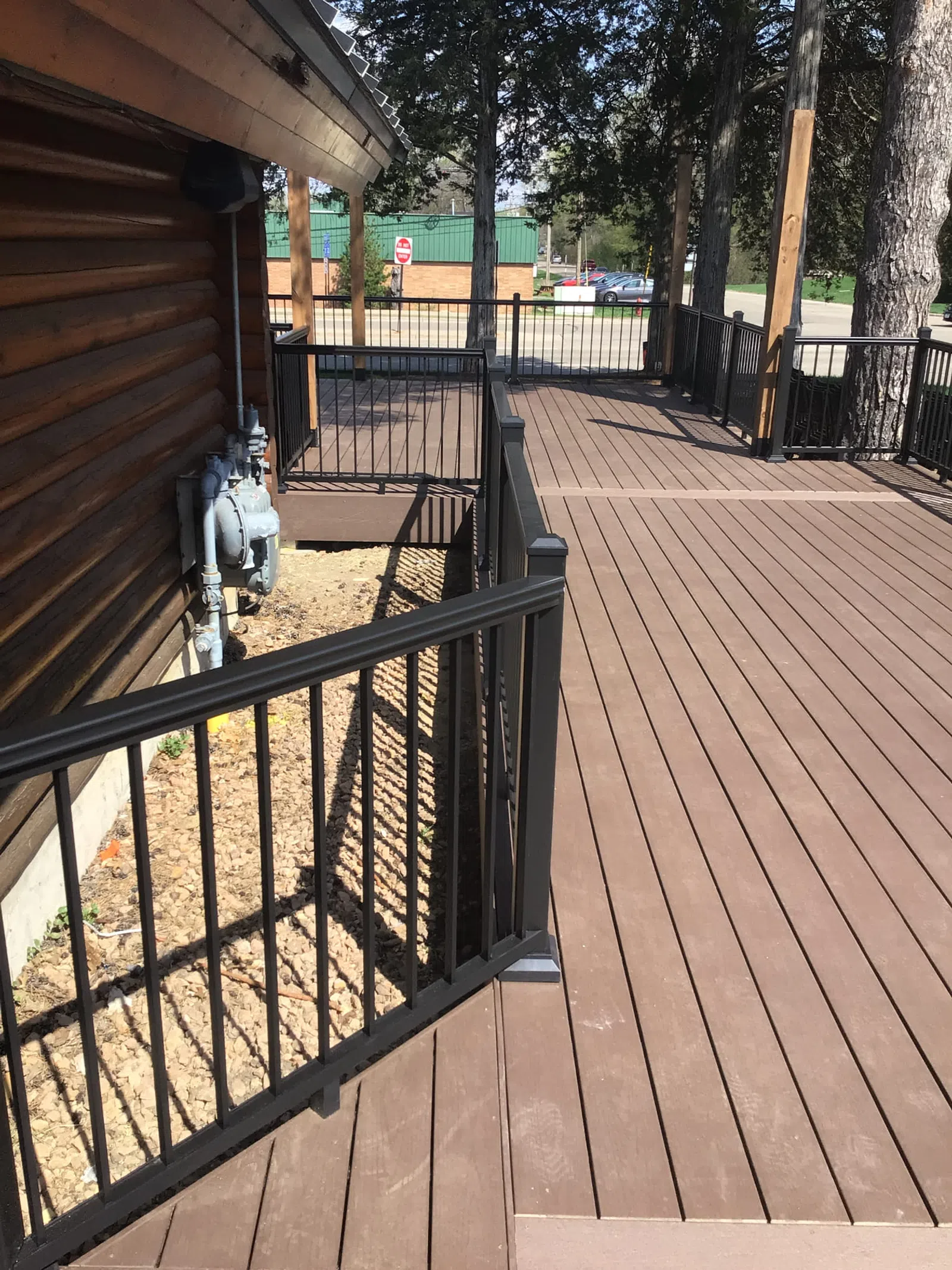 Spacious brown wooden deck with black metal railings next to a log cabin and trees in the background.