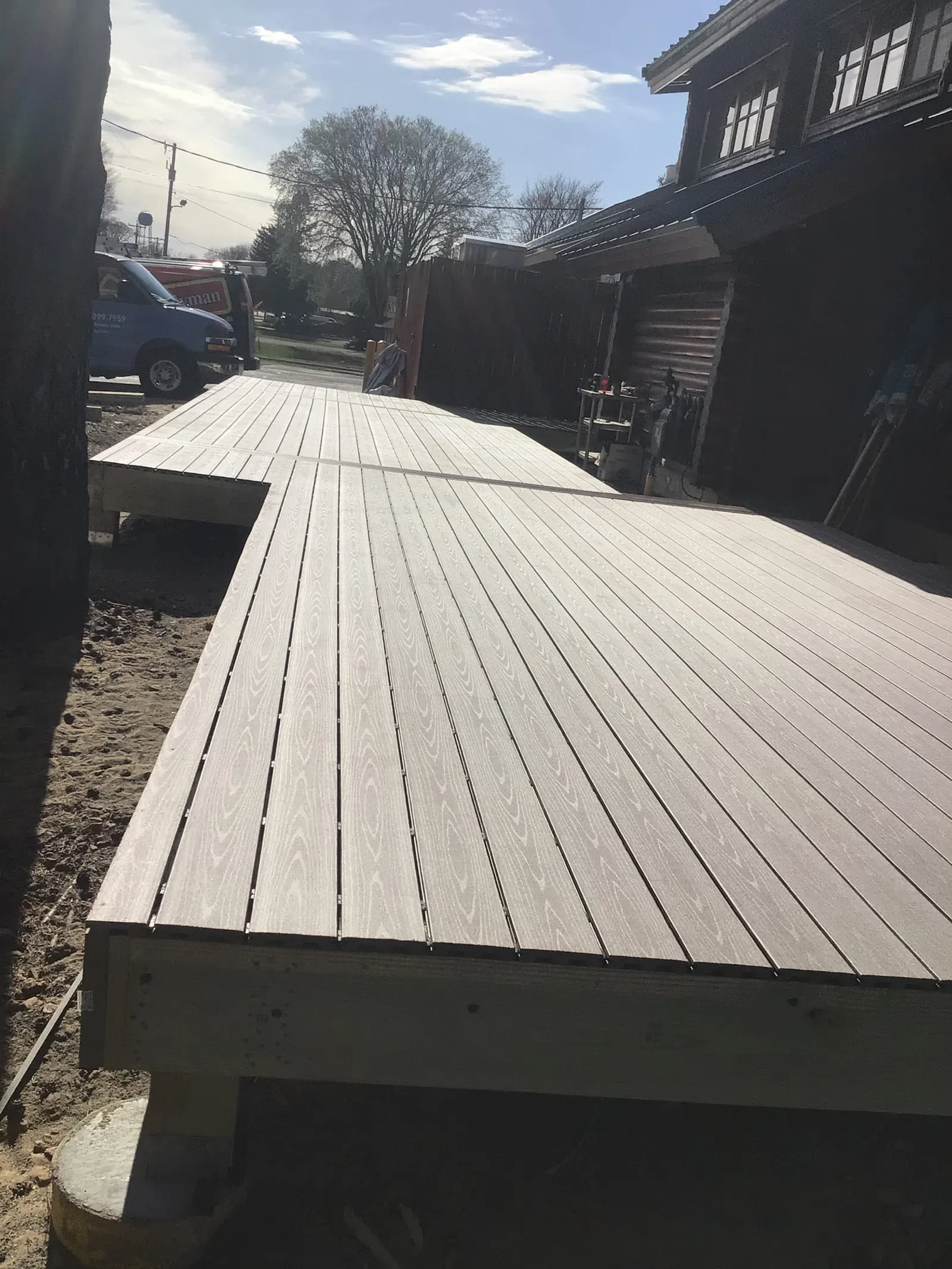 Newly constructed brown wooden deck extending from a house under a partly cloudy sky.