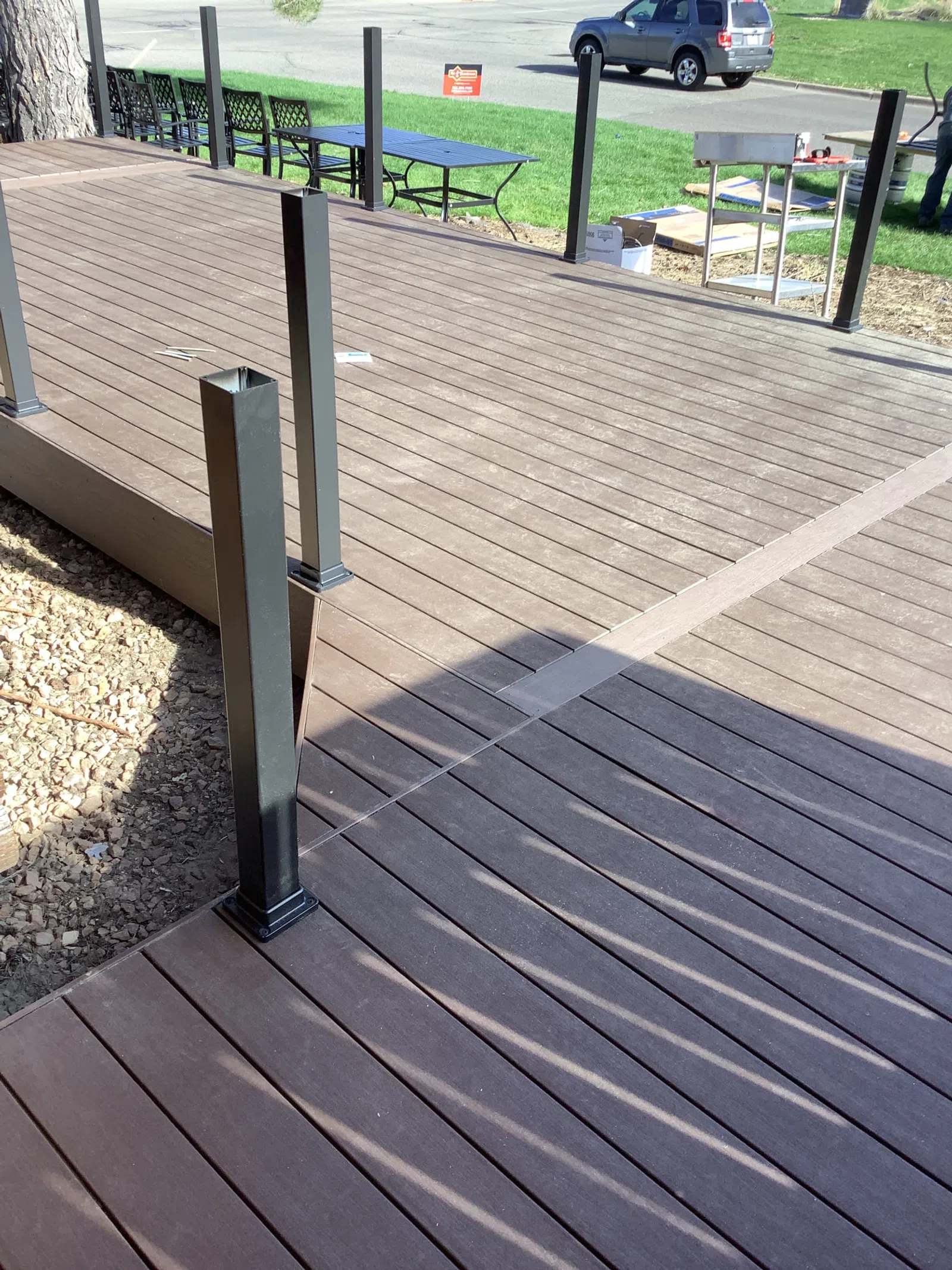 Newly constructed brown composite wood deck with metal posts for railing under sunlight in outdoor setting.