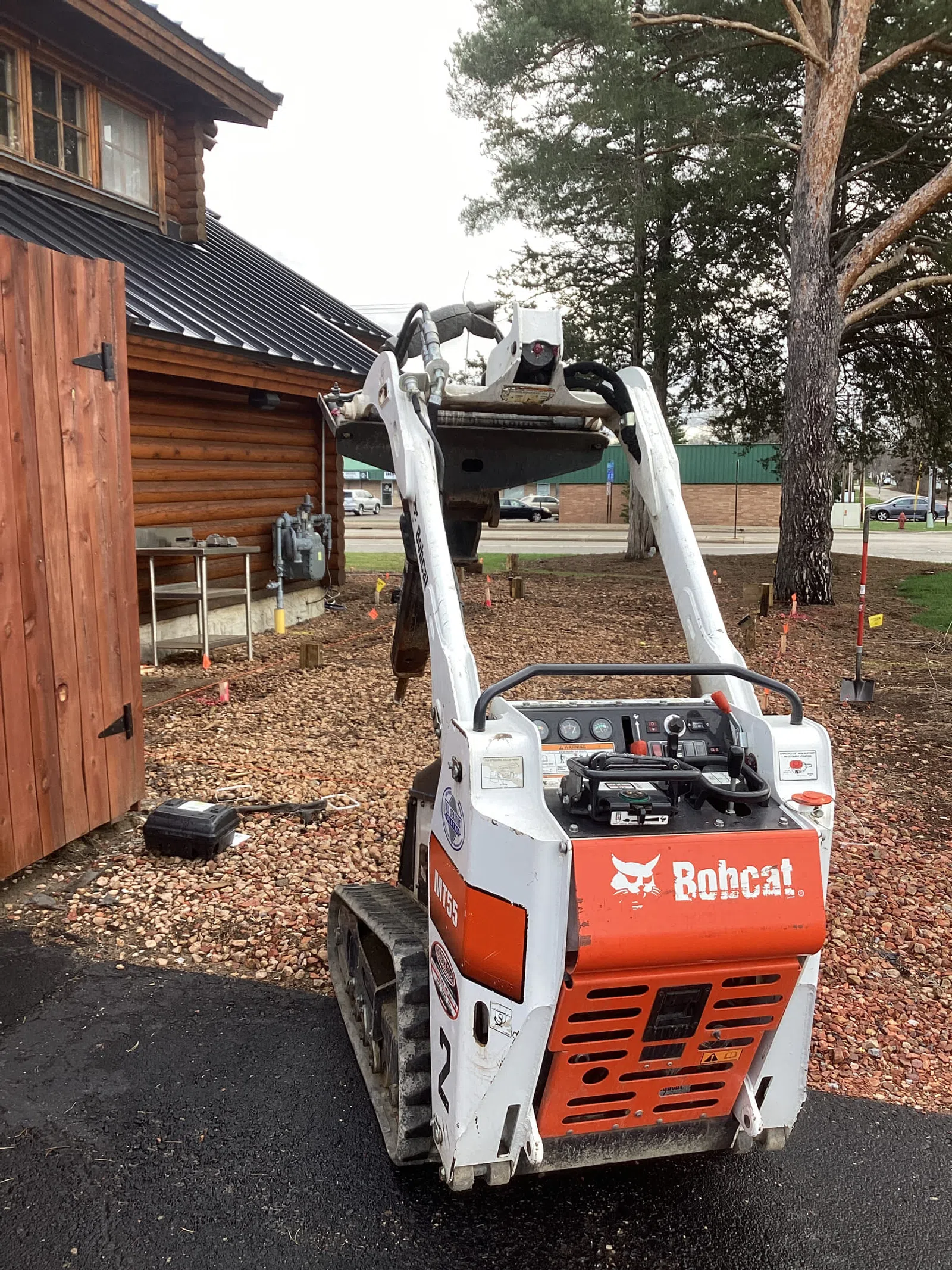 Compact Bobcat MT55 mini track loader parked near a wooden cabin on a construction site.
