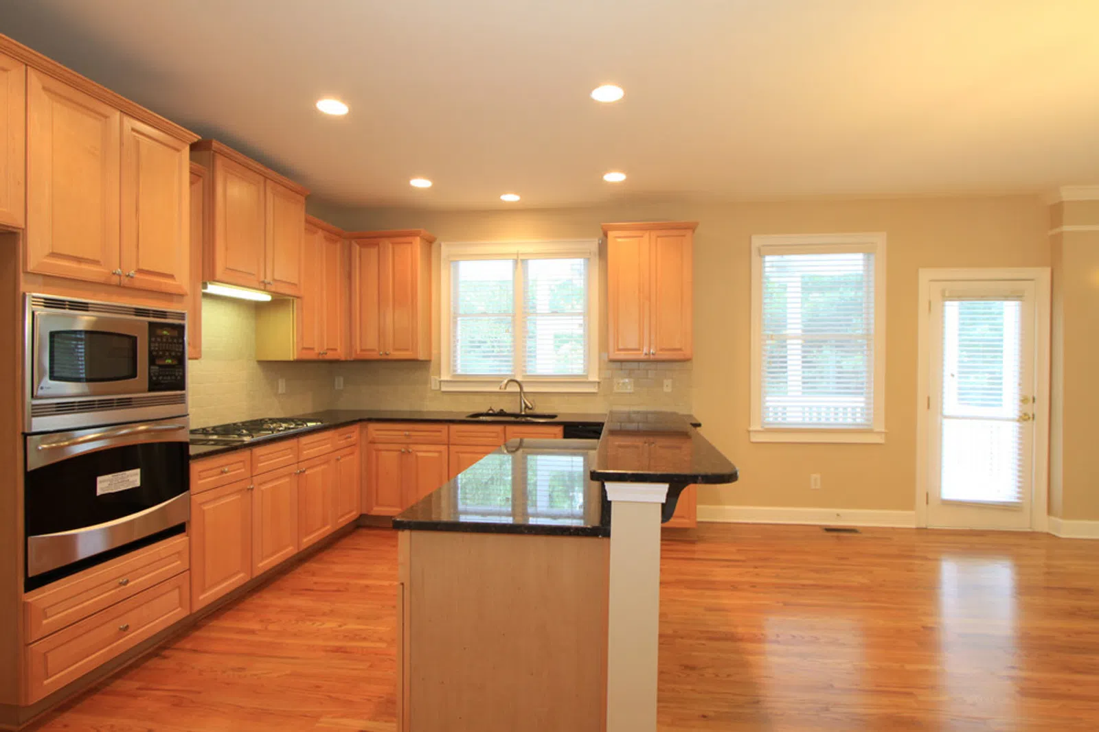 Bright spacious kitchen with wooden cabinets, granite countertops, hardwood floors, and stainless steel appliances.