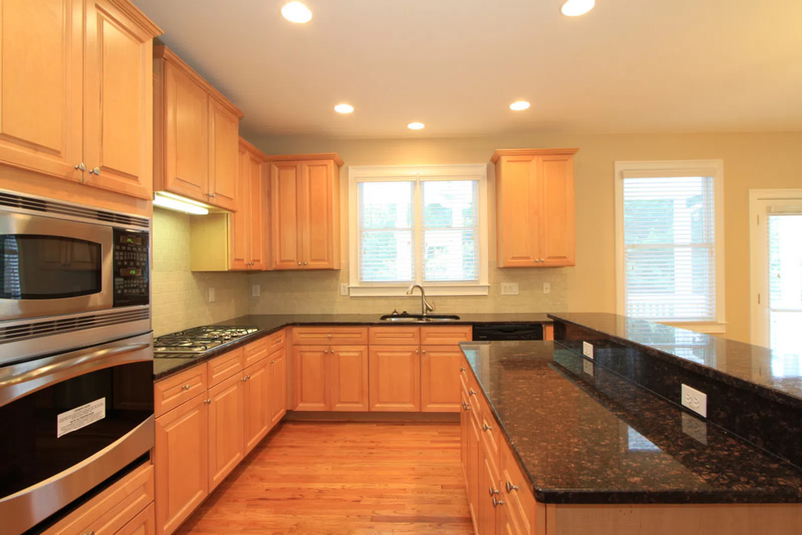 Modern kitchen with wooden cabinets, black granite countertops, stainless steel appliances, and hardwood flooring.