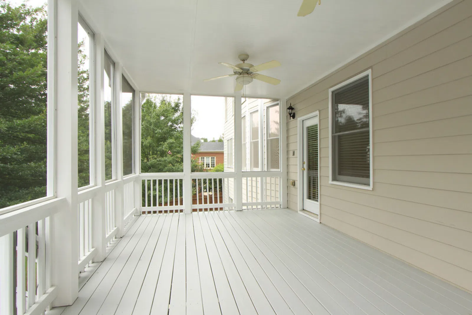 Bright spacious screened porch with white railing, ceiling fan, beige siding, and natural outdoor view.