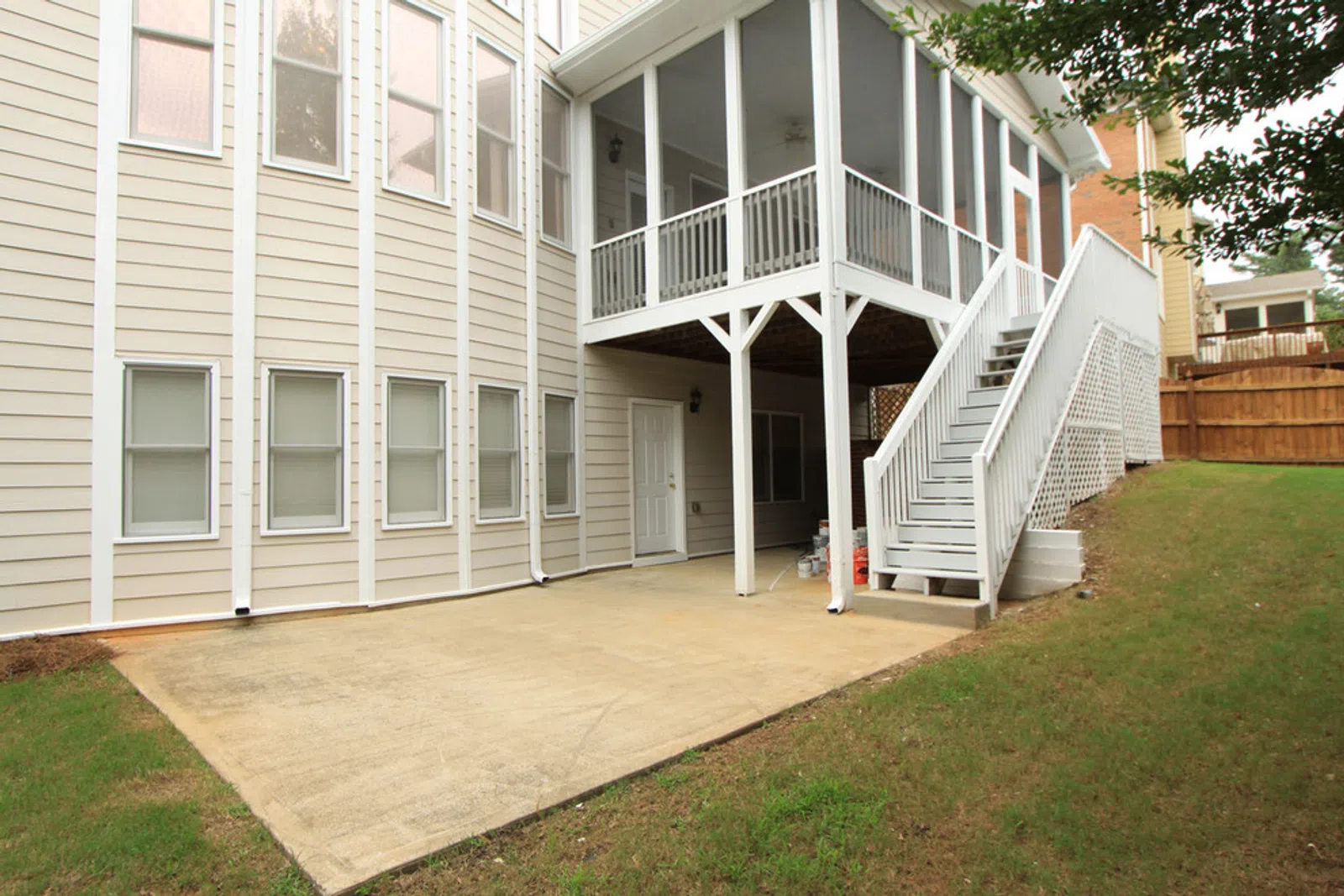 House exterior with beige siding, concrete patio, white screened porch, and stairs leading to backyard.