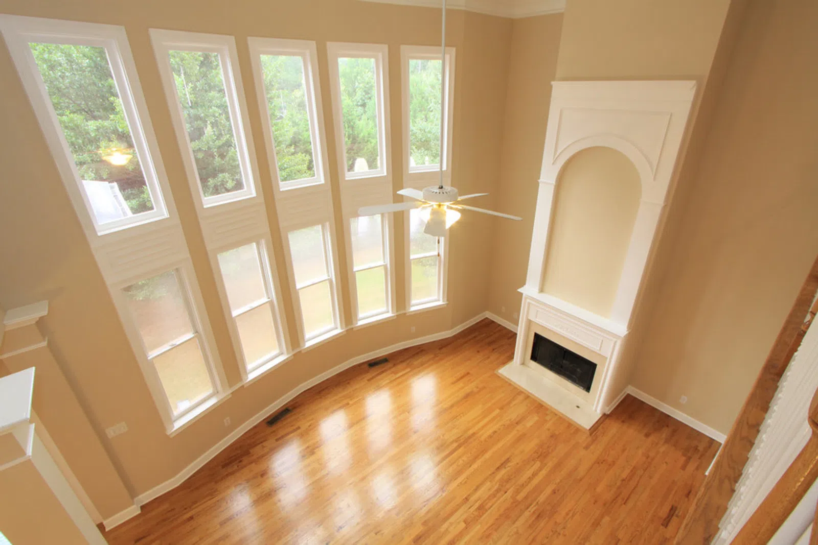 Bright spacious living room with tall windows, hardwood floors, and a white fireplace under high ceilings.