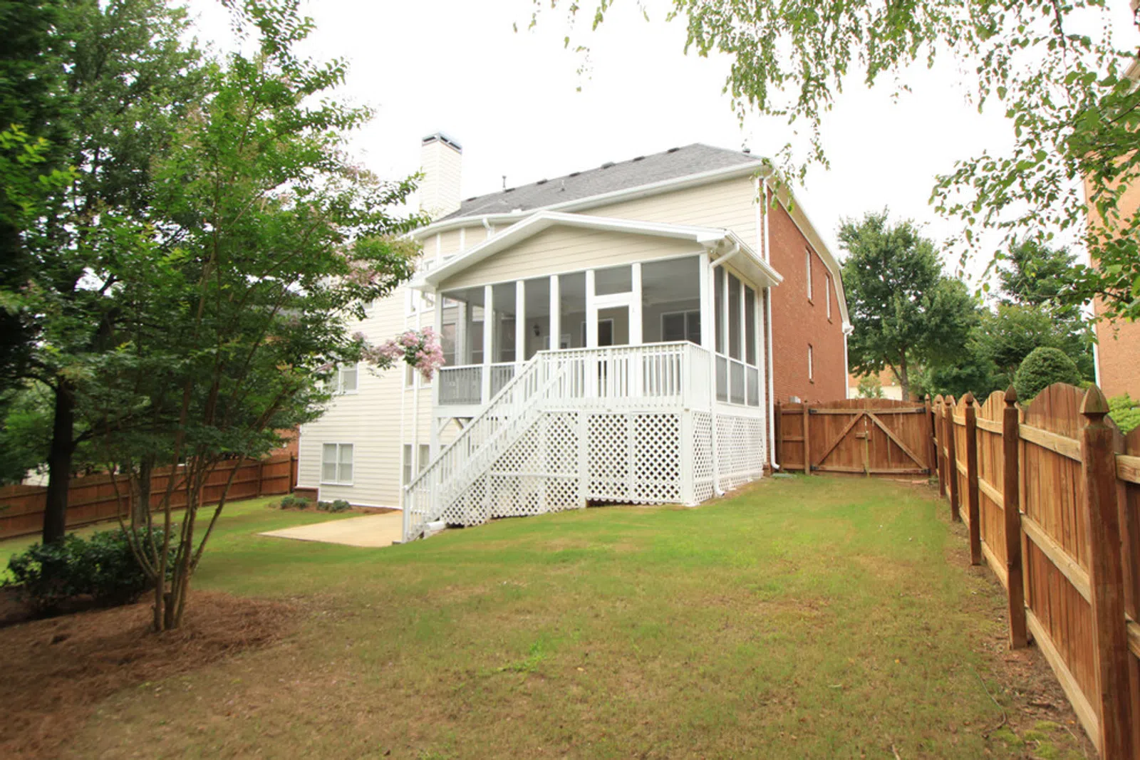 Backyard view of a house with a white screened porch and wooden fence surrounding the grassy yard.