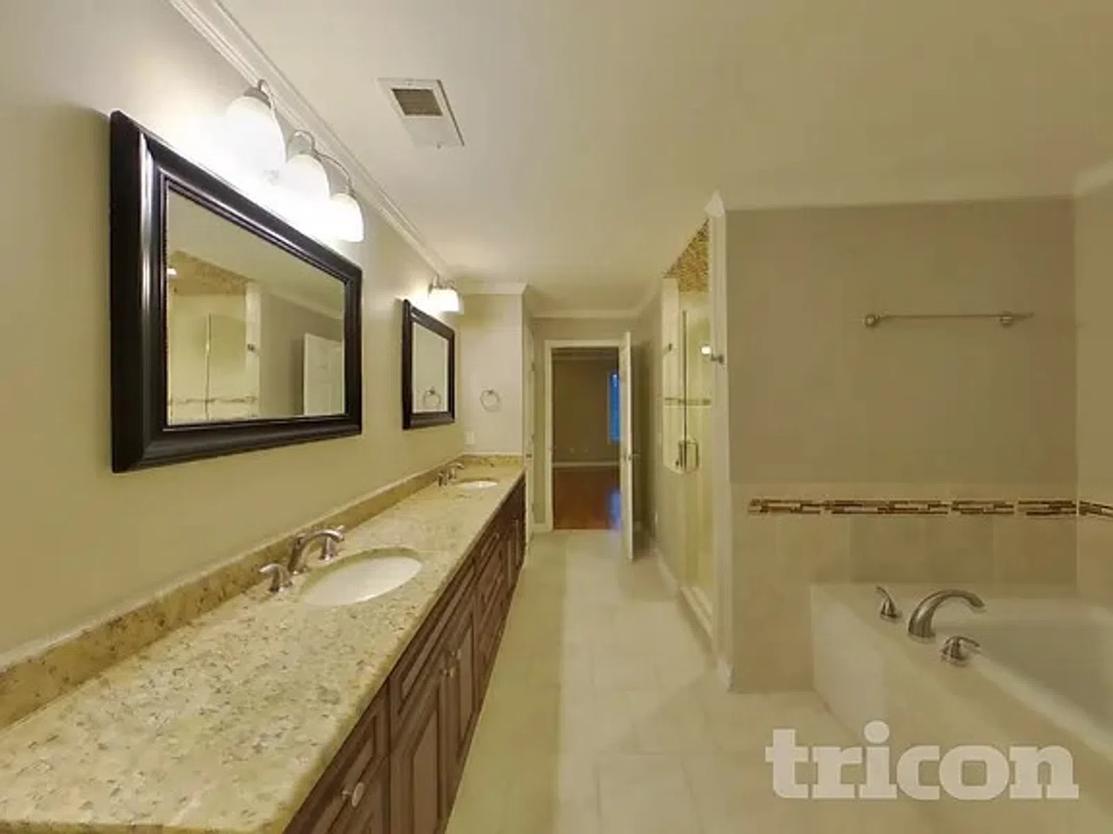 Spacious bathroom with double sink granite countertop, large mirrors, bathtub, and glass shower enclosure.