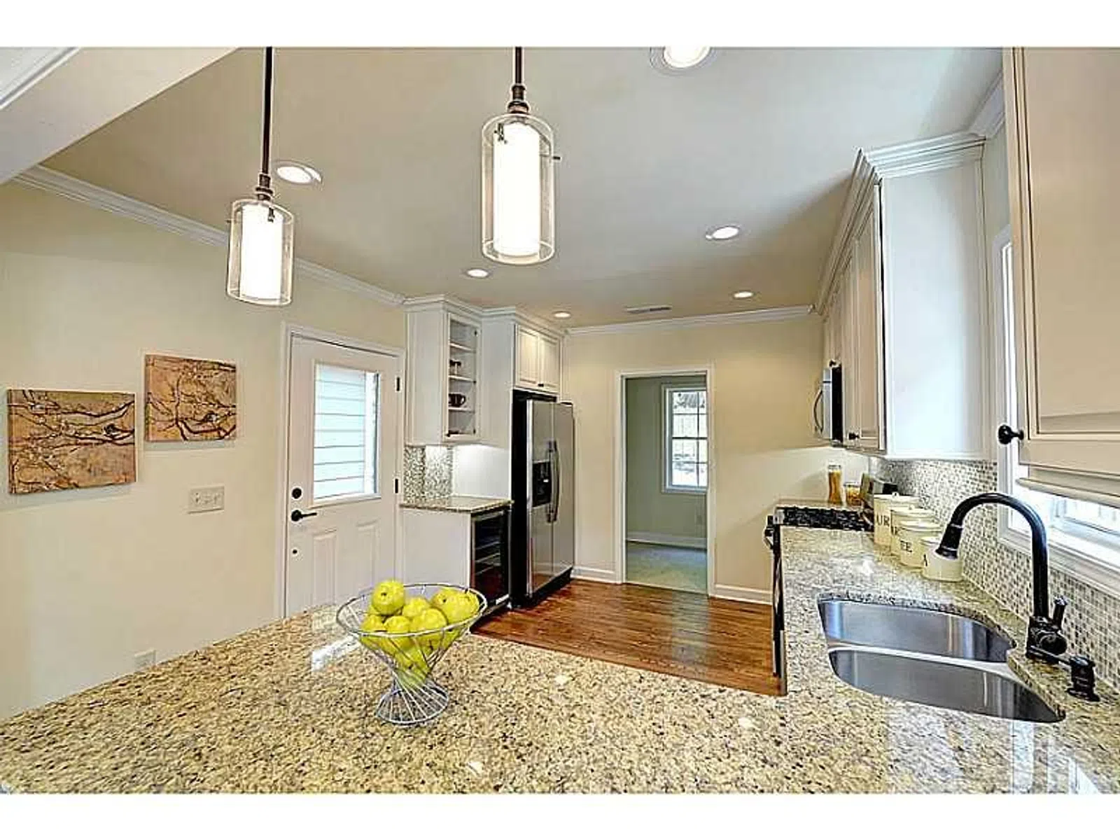 Modern kitchen with granite countertops, stainless steel appliances, pendant lighting, and hardwood floors.