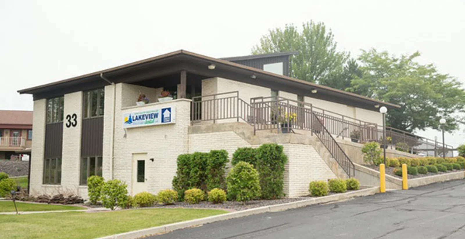 Modern two-story Lakeview building with stairs, railings, greenery, and a parking lot under an overcast sky