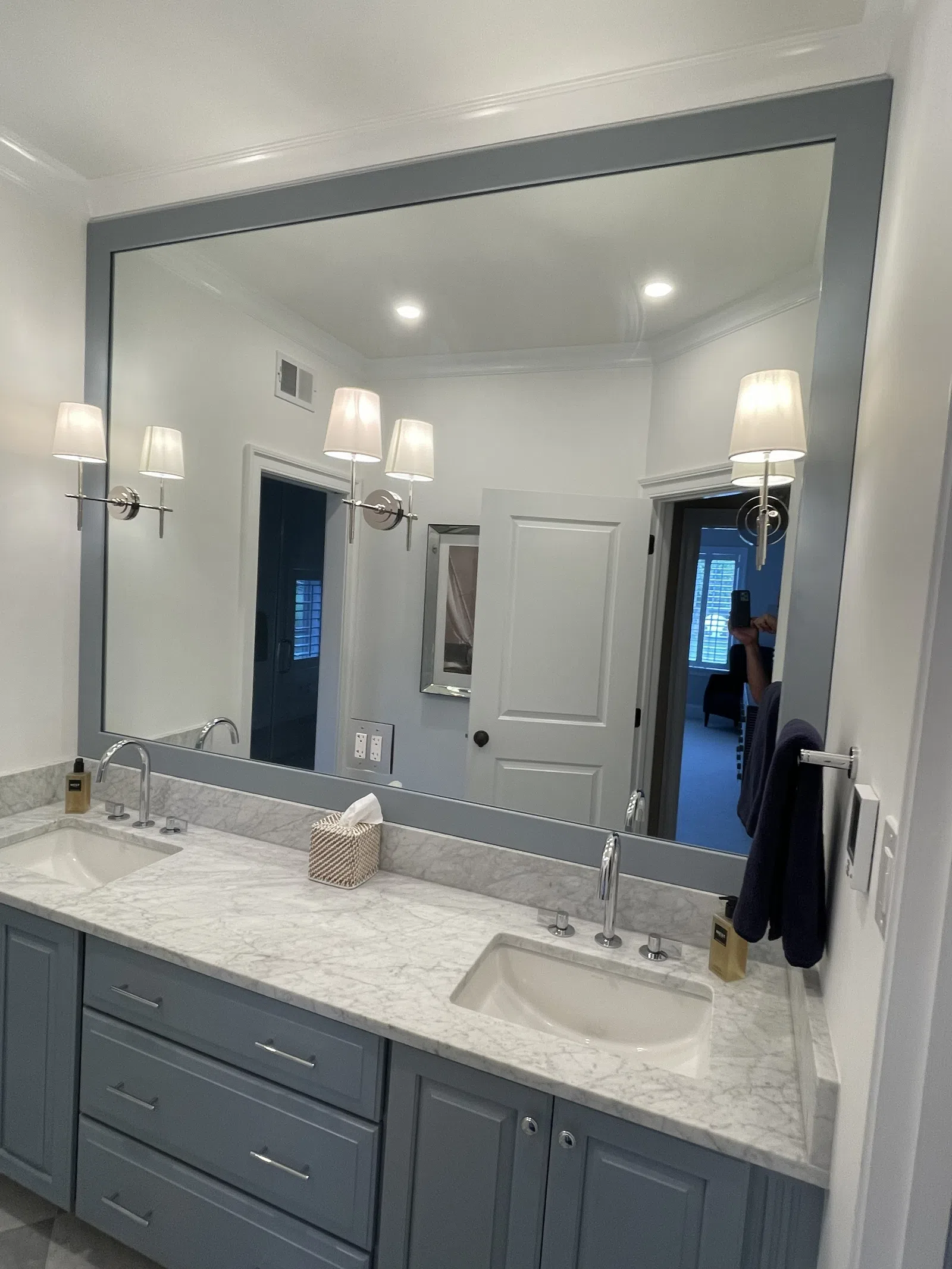 Modern bathroom vanity with double sinks, marble countertop, large gray framed mirror, and wall-mounted lights.
