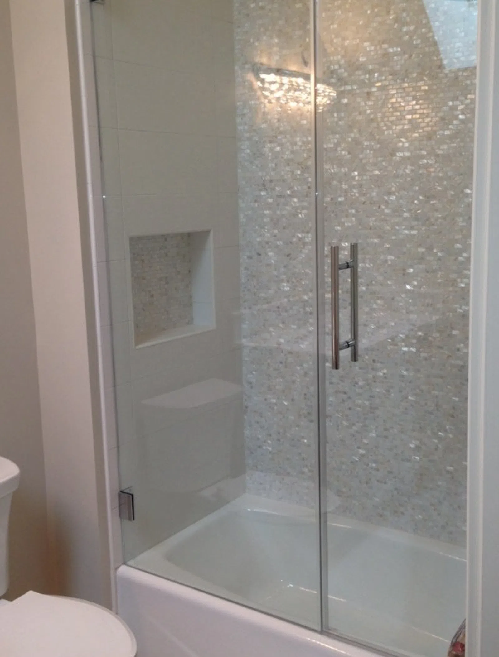 Modern bathroom shower with glass sliding doors and mosaic tile wall inside the tub area.
