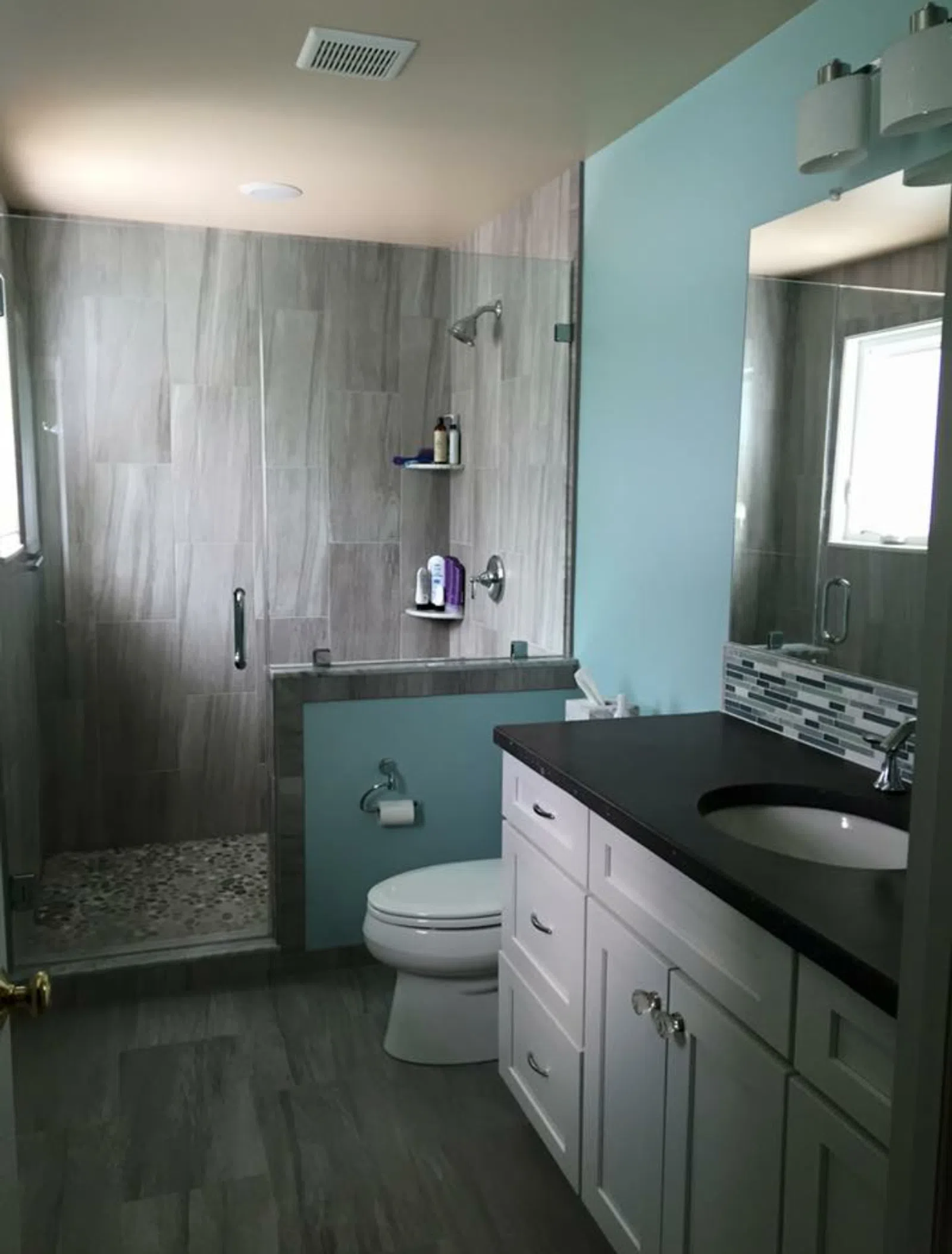 Modern bathroom with glass shower, light blue walls, white vanity, and dark countertop with large mirror.