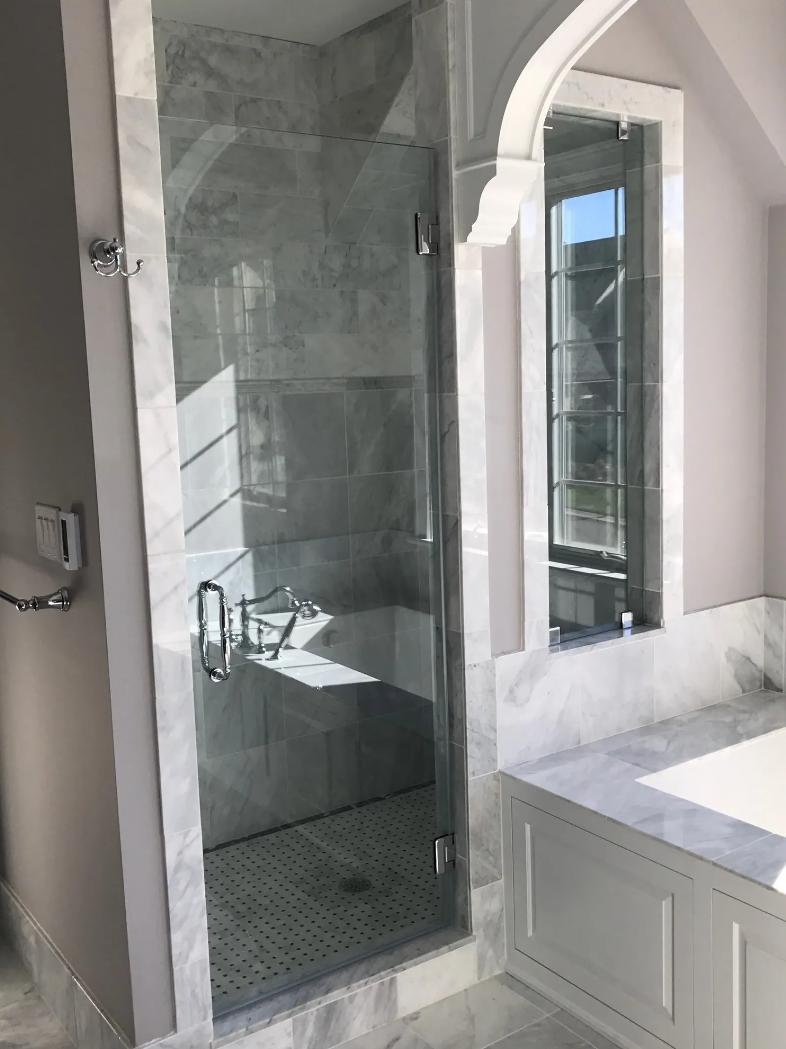 Modern bathroom with glass shower enclosure, marble tiles, built-in bathtub, and large window.