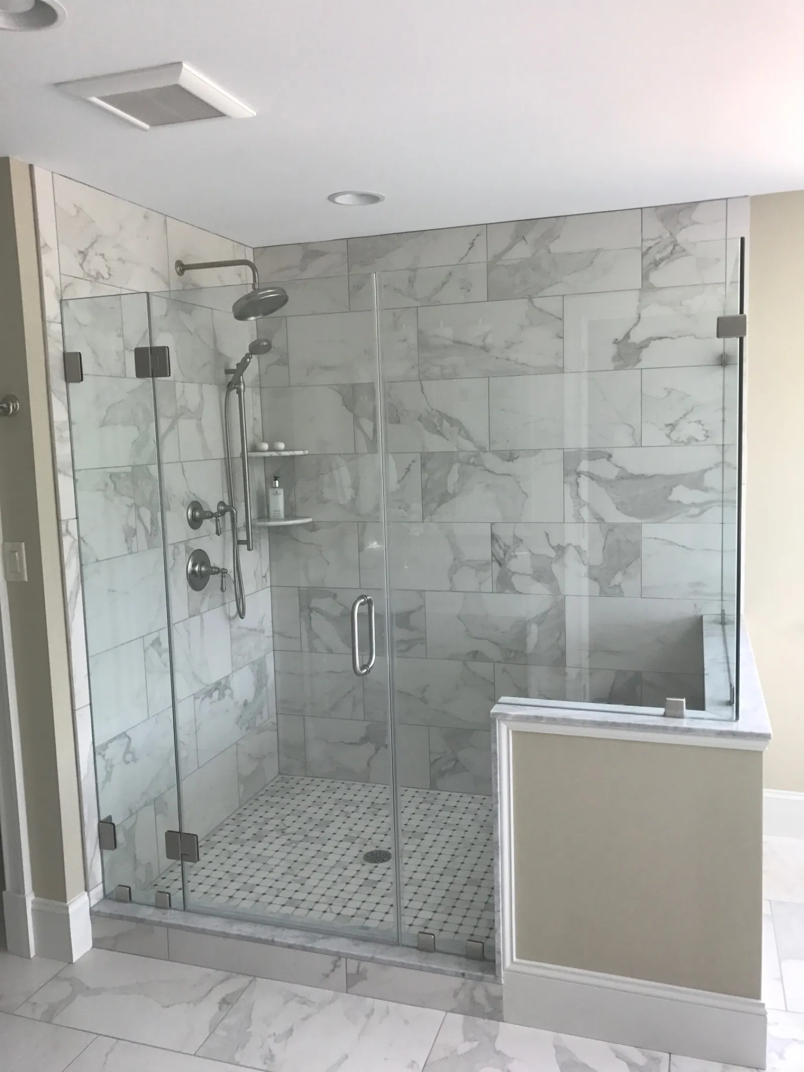 Modern glass-enclosed walk-in shower with marble tiles and rain showerhead in a bright bathroom.