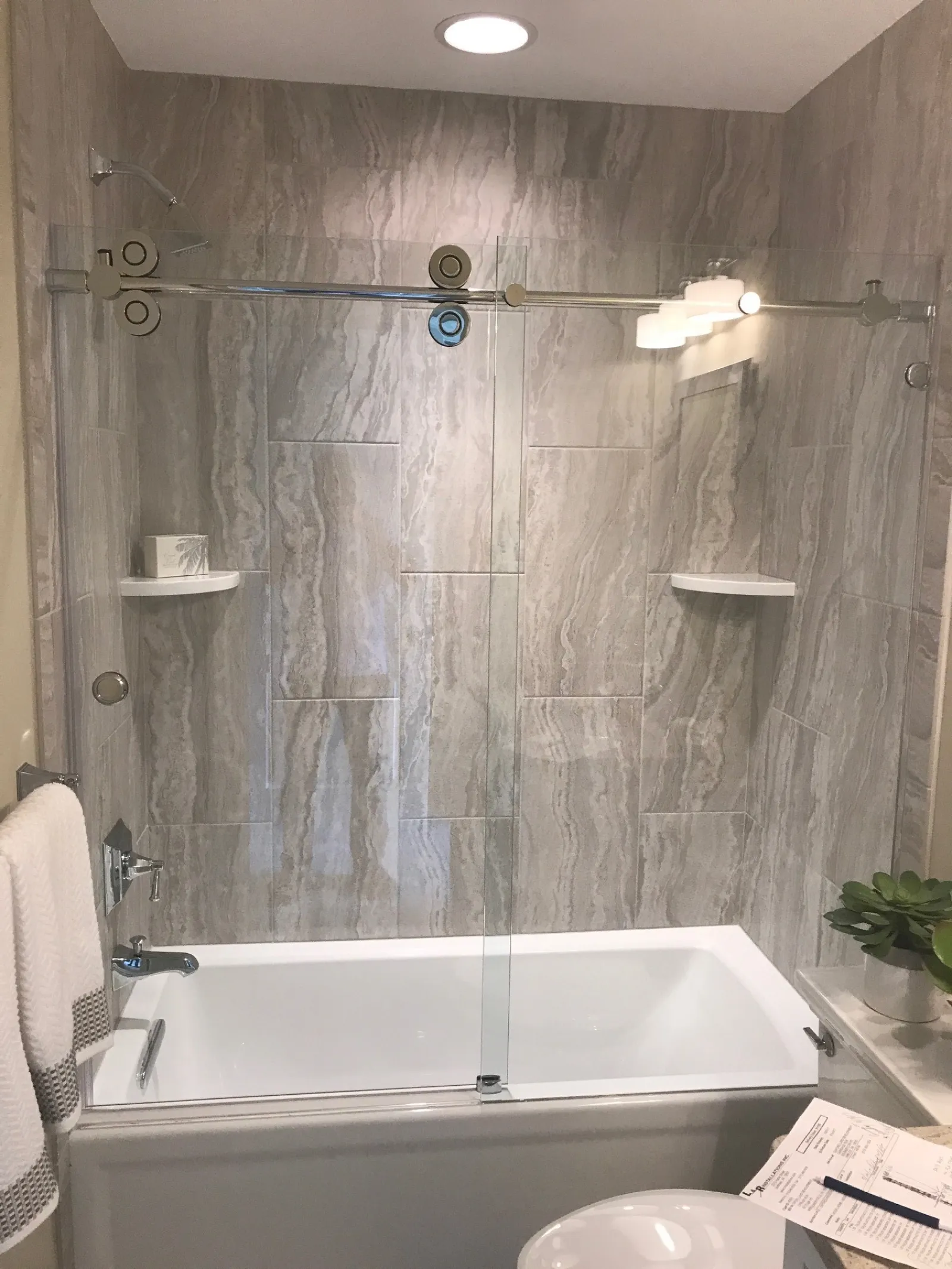 Modern bathroom with a white bathtub, glass sliding door, marble wall tiles, and towels on a rack.