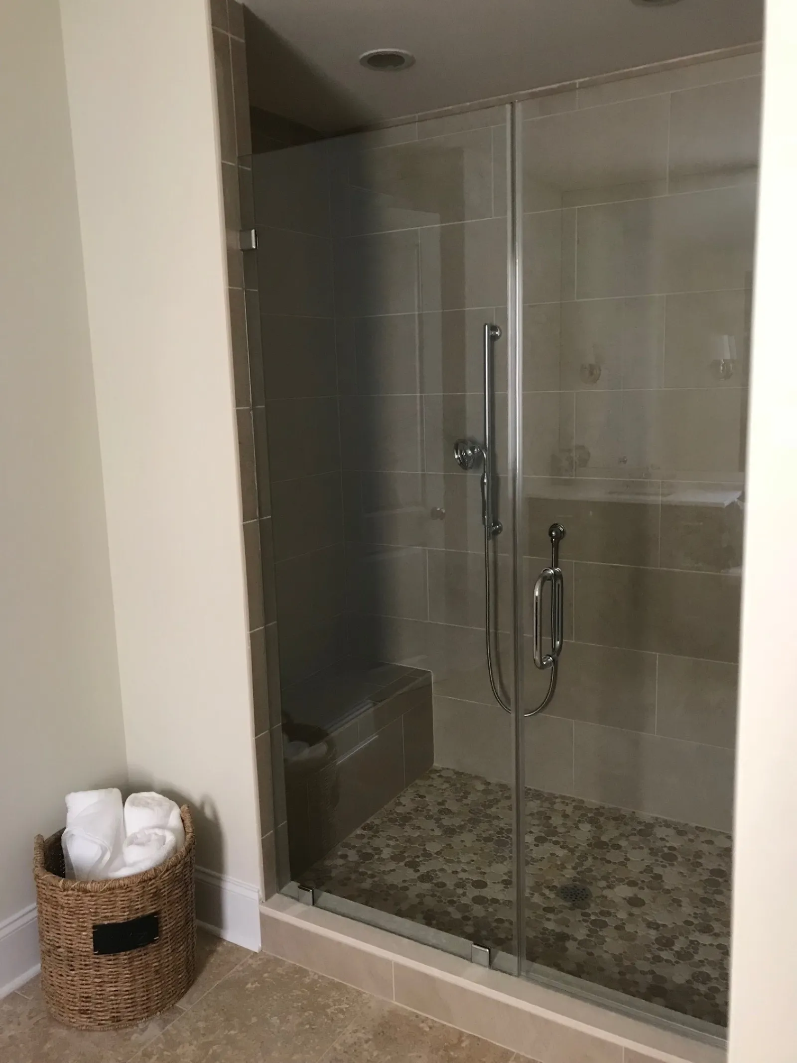Modern tiled walk-in shower with glass doors, built-in bench, and a wicker basket with white towels nearby.