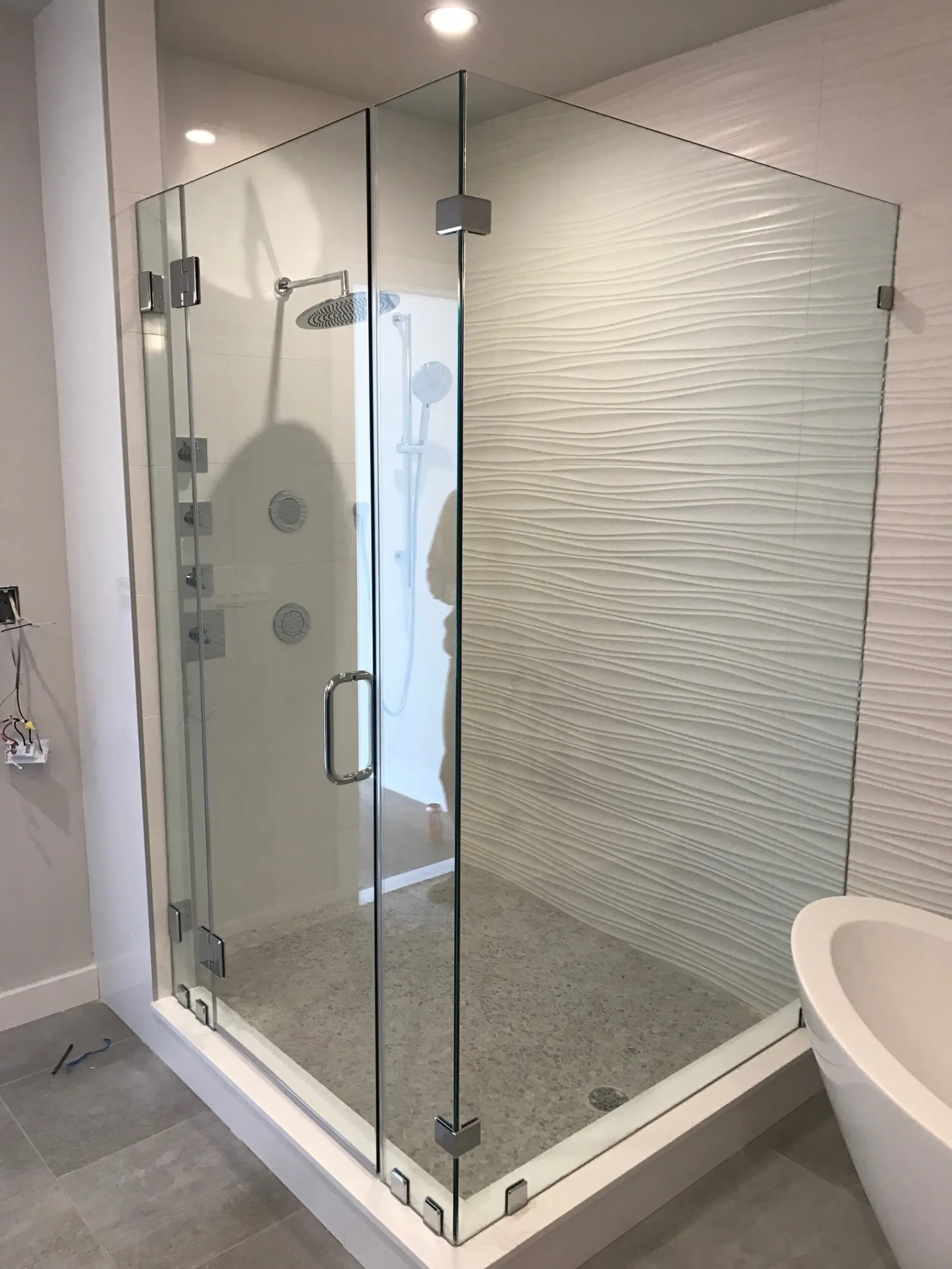 Modern bathroom with glass shower enclosure, textured wall tiles, rain showerhead, and freestanding bathtub.