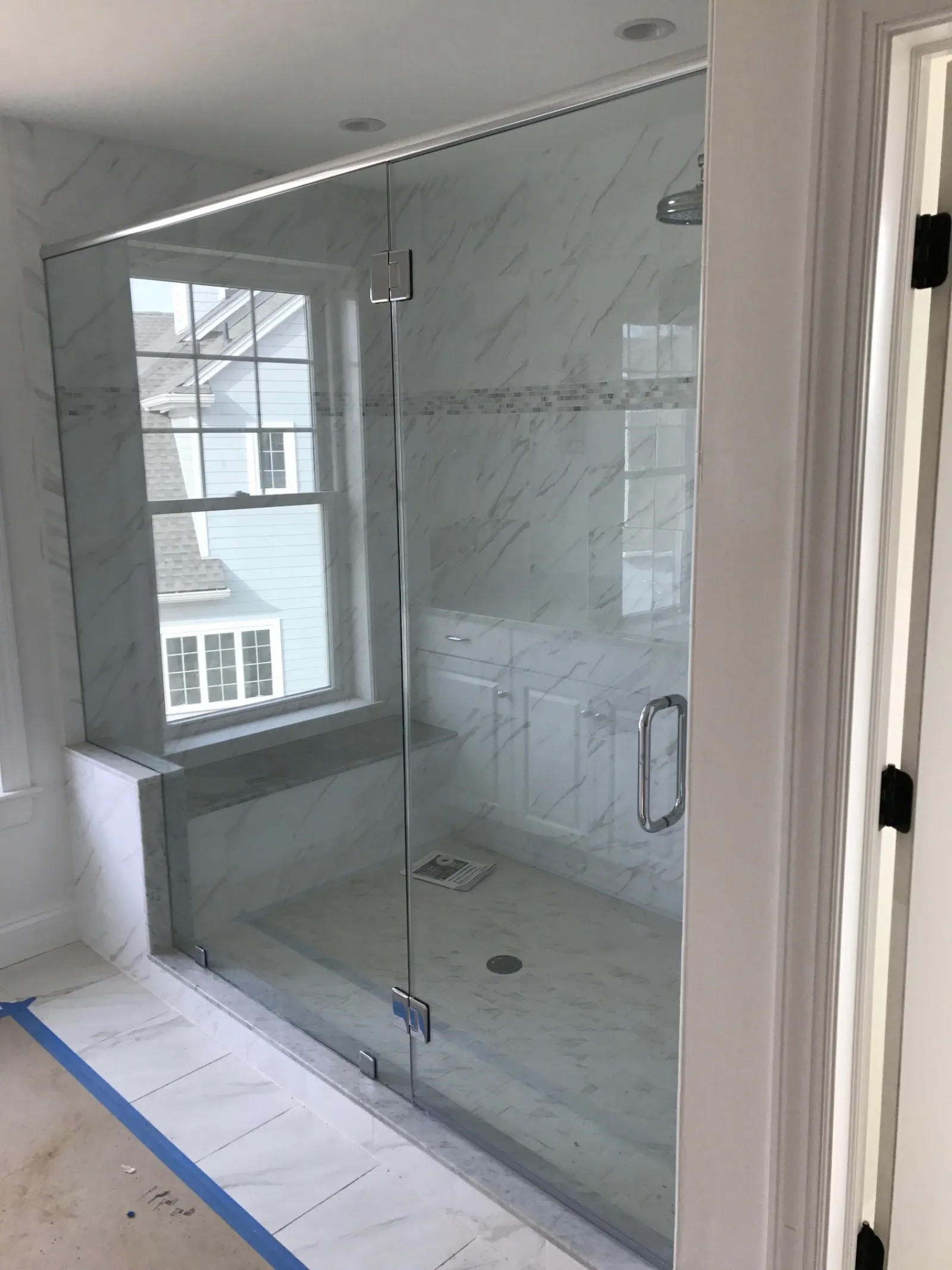 Modern bathroom with a frameless glass shower enclosure and marble-patterned tiles inside and out.