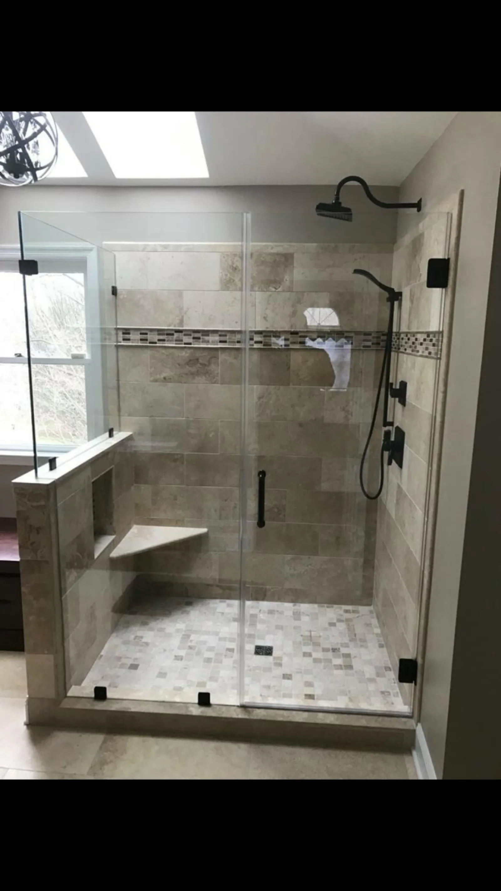 Modern tiled walk-in shower with glass enclosure, built-in bench, and black fixtures in natural stone colors.