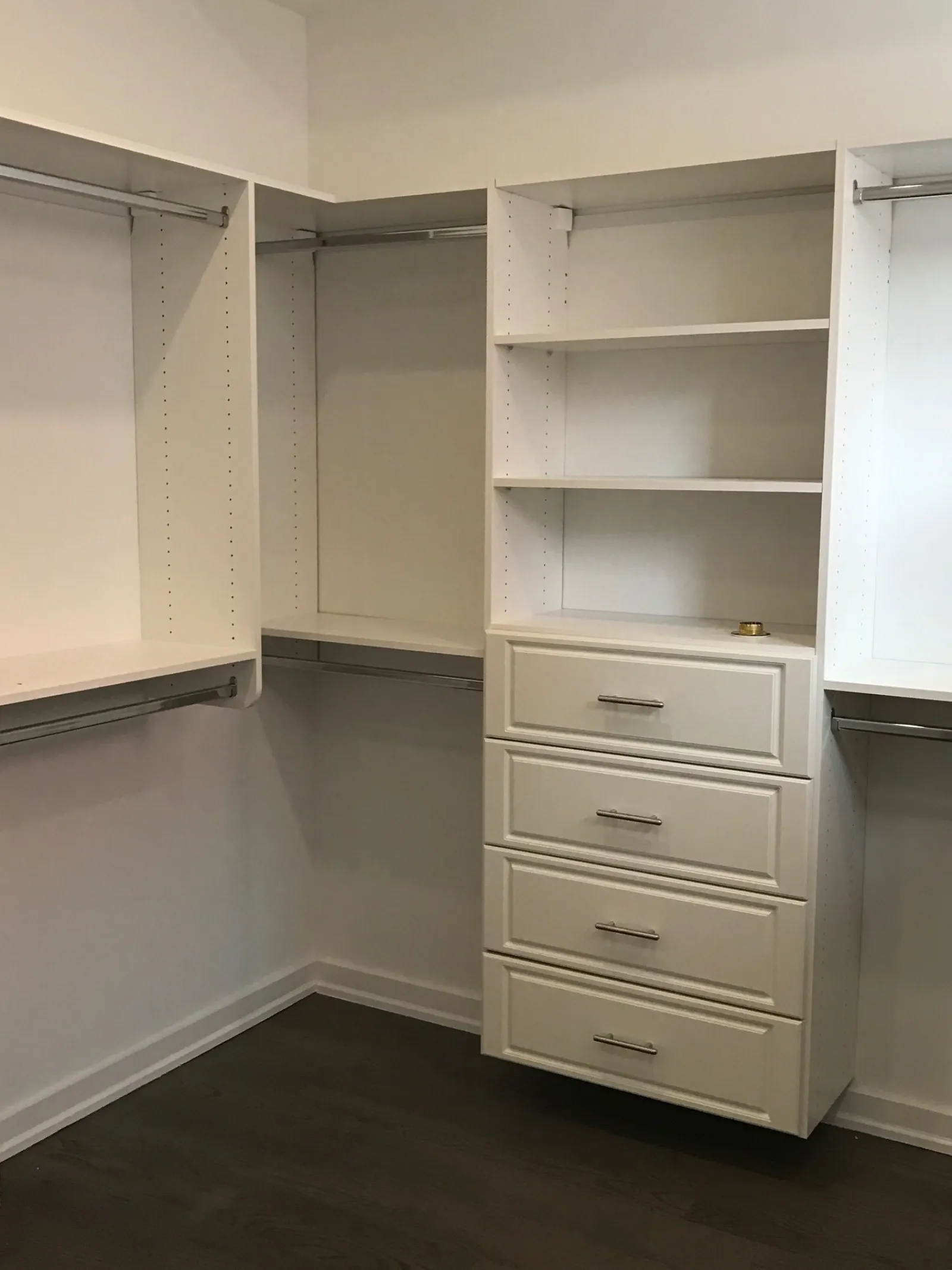Empty white walk-in closet with built-in shelves, drawers, and hanging rods on dark wood flooring