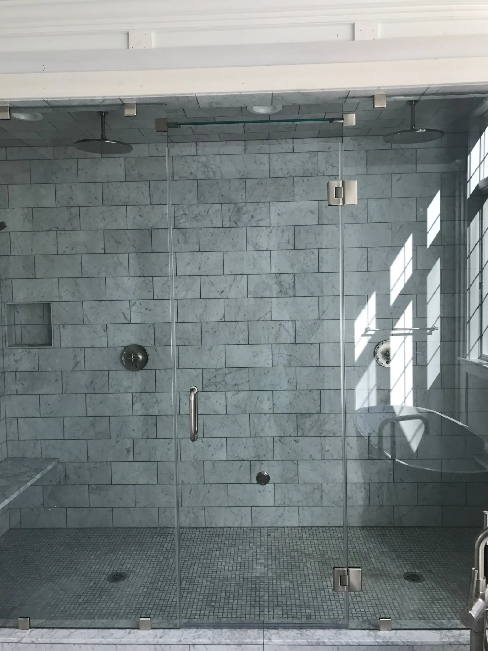Spacious modern glass shower with marble tiles, dual showerheads, and natural light through window.