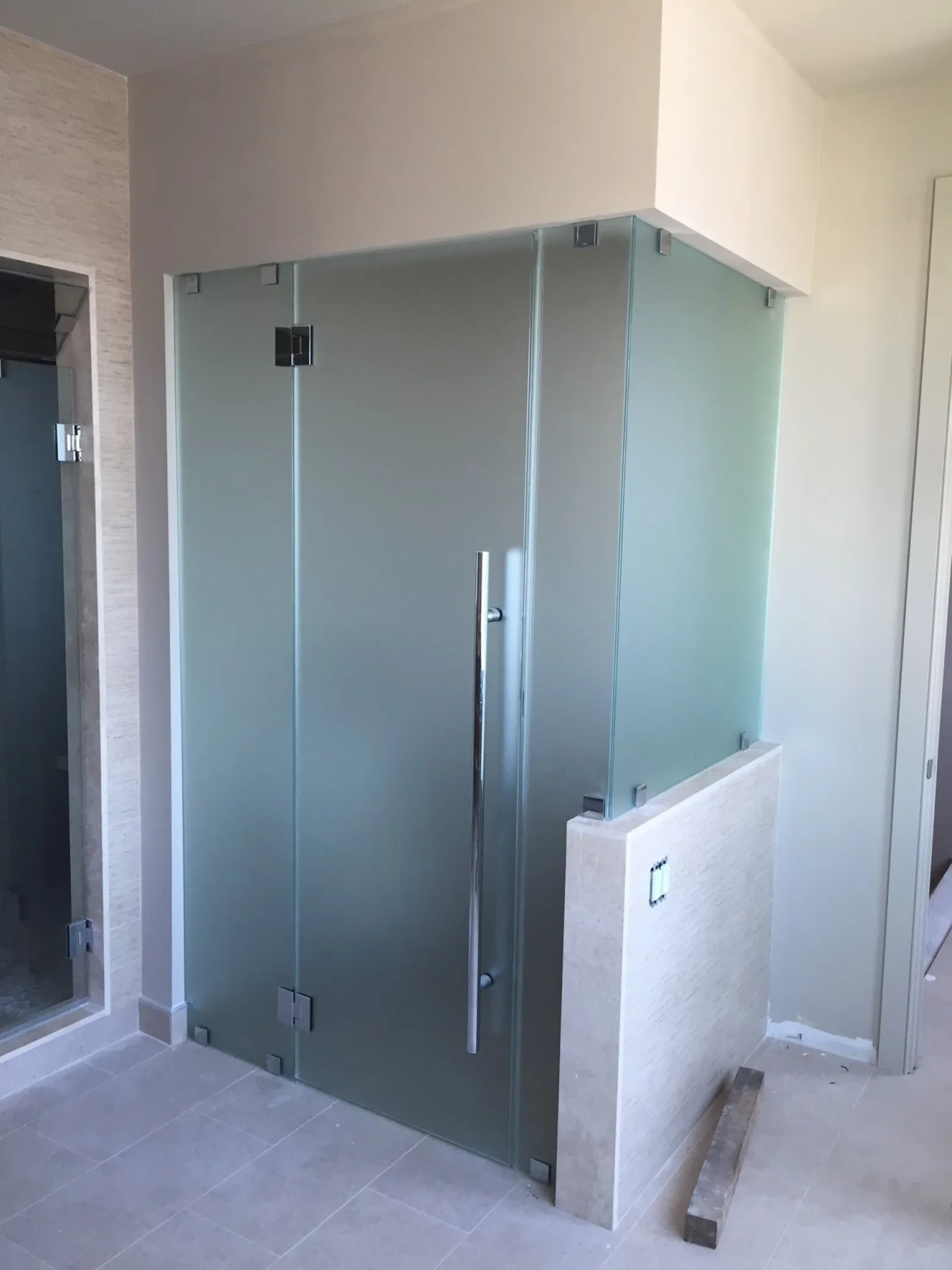 Modern bathroom corner with frosted glass shower enclosure and chrome handle on light tile floor.