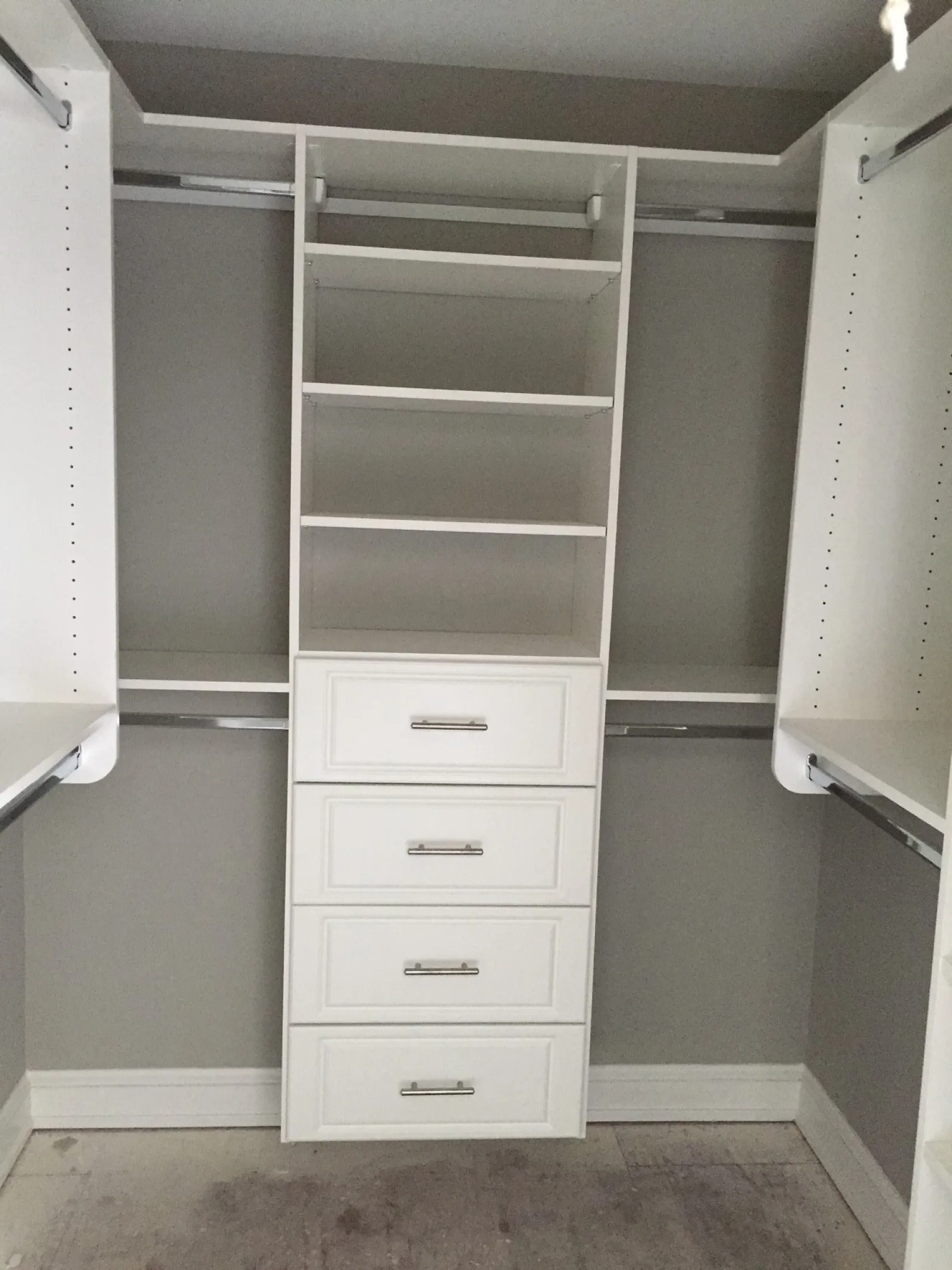 Empty white walk-in closet with built-in shelves, drawers, and hanging rods against gray walls.