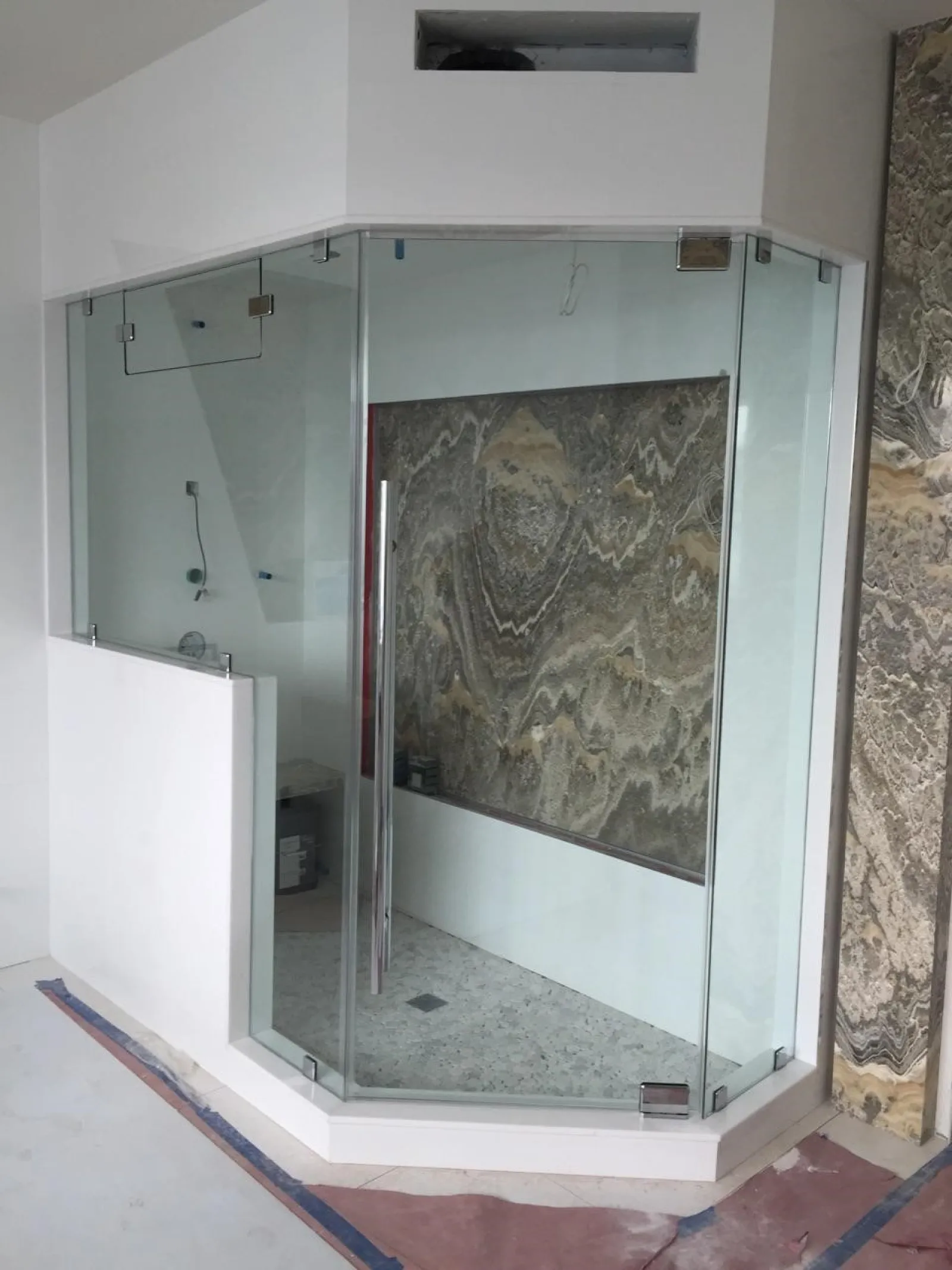 Modern frameless glass shower enclosure with stone tile walls and floor under construction in bathroom.