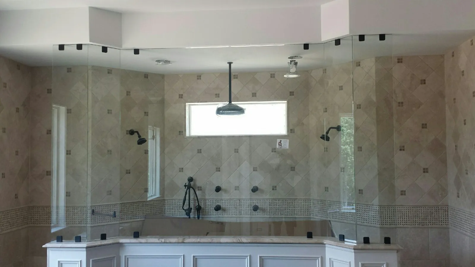 Modern bathroom with large frameless glass shower enclosure, multiple showerheads, and beige tiled walls.