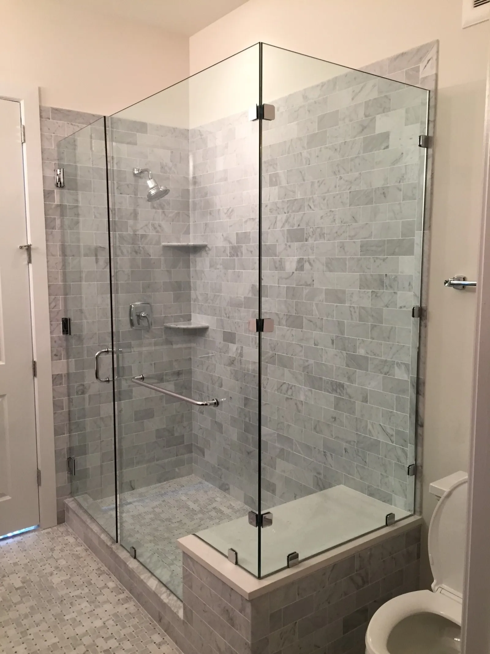 Modern bathroom with glass-enclosed shower, gray mosaic tiles, and stainless steel fixtures including showerhead and grab bar