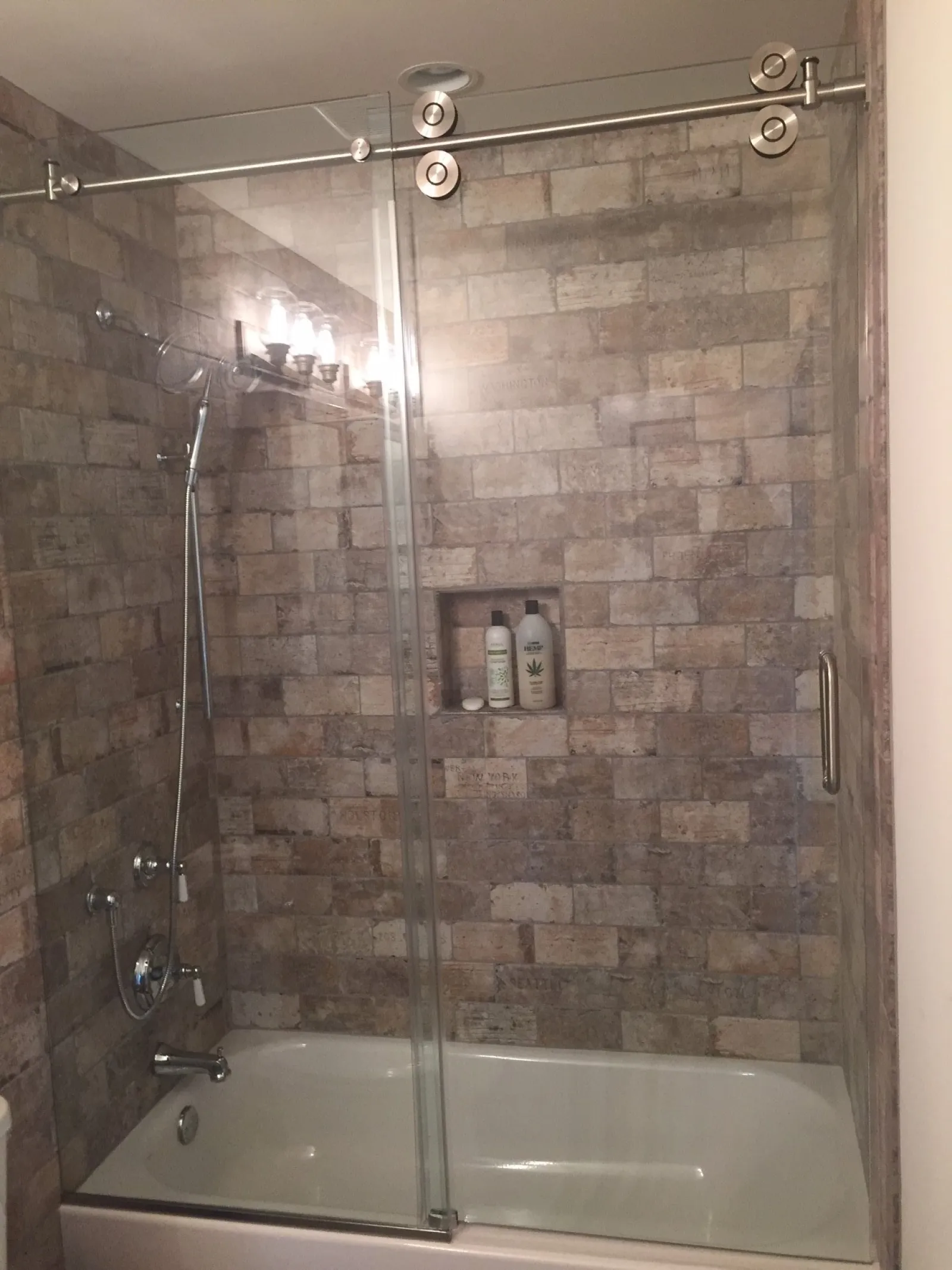 Modern bathroom with a bathtub, stone tile walls, glass sliding shower doors, and built-in shampoo niche.