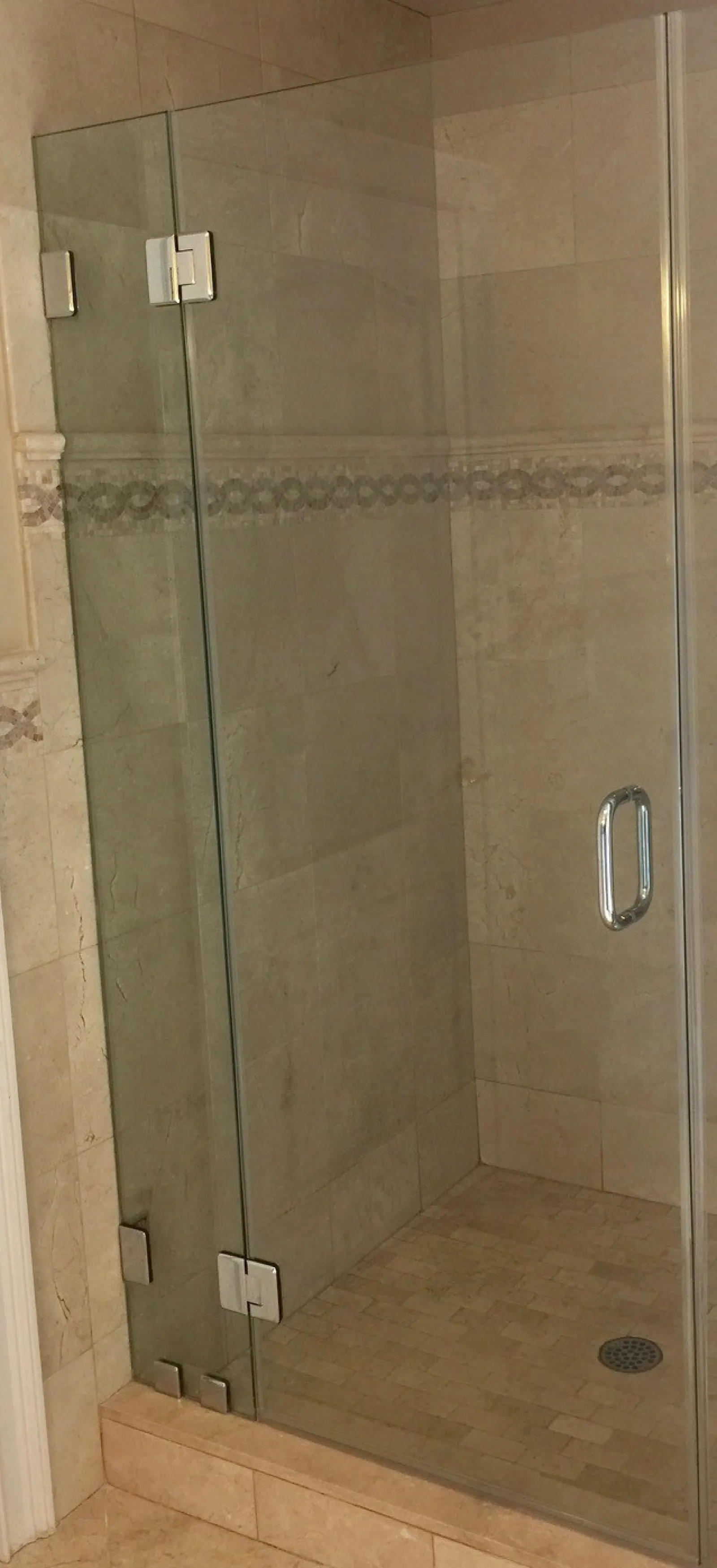 Modern walk-in shower with glass door and beige tiled walls and floor with decorative border
