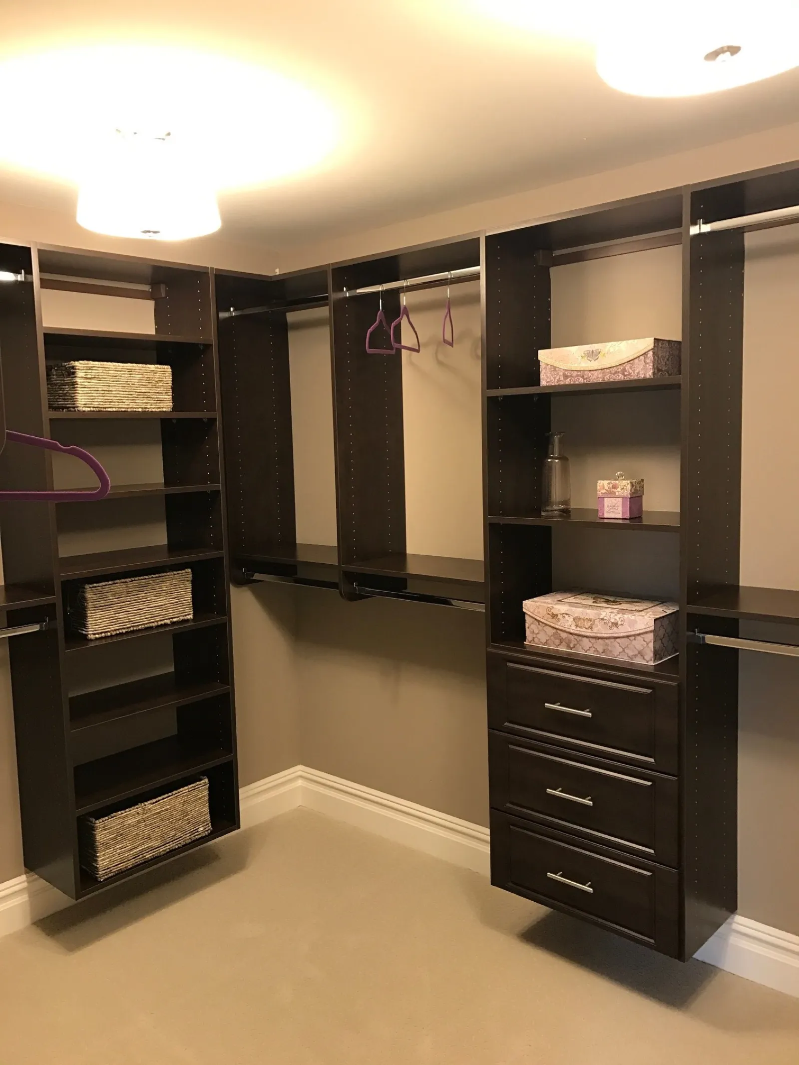 Spacious walk-in closet with dark wood shelves, drawers, hanging rods, baskets, and decorative boxes
