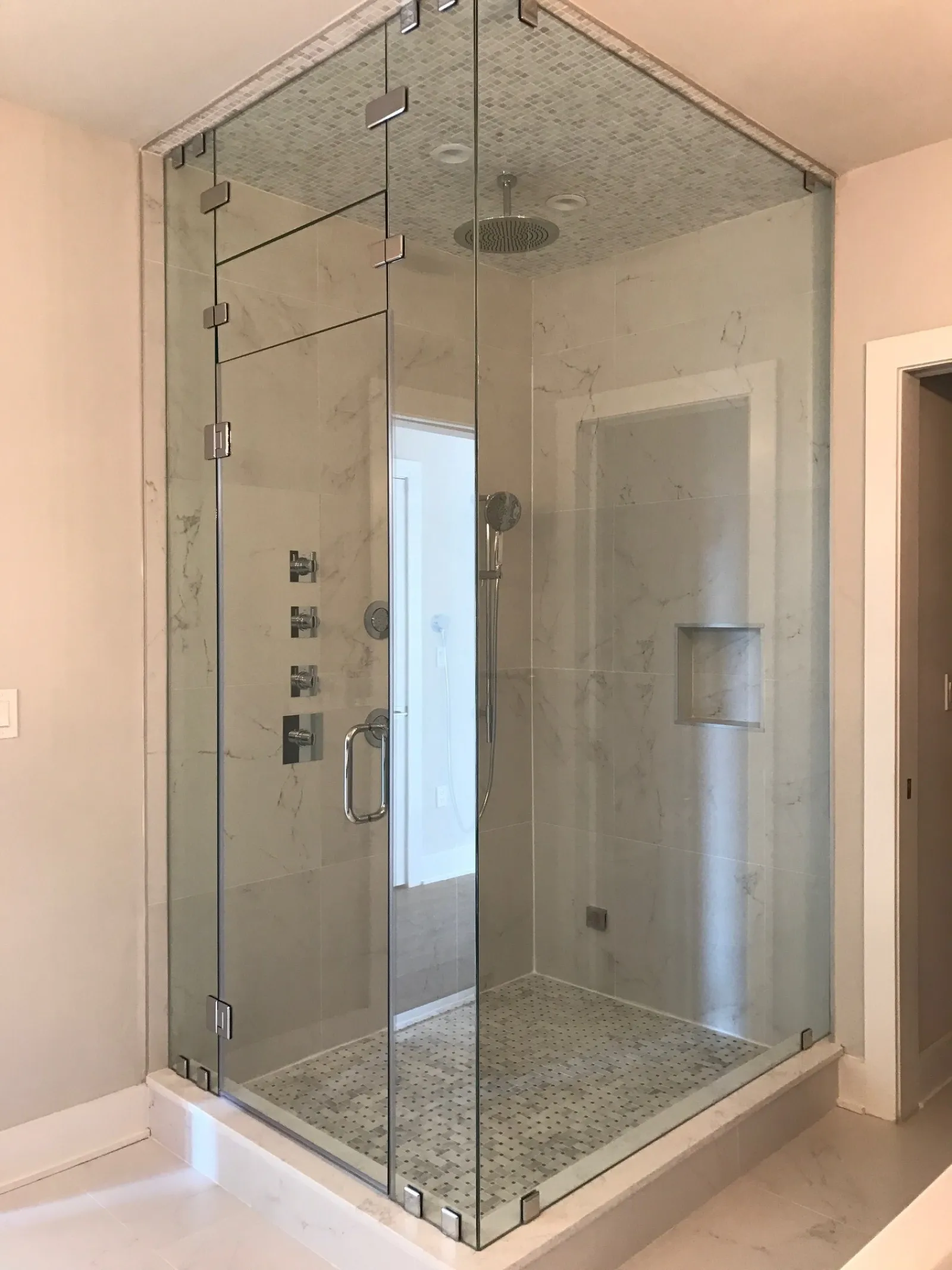 Modern frameless glass shower enclosure with marble tile walls and rain showerhead in a bathroom